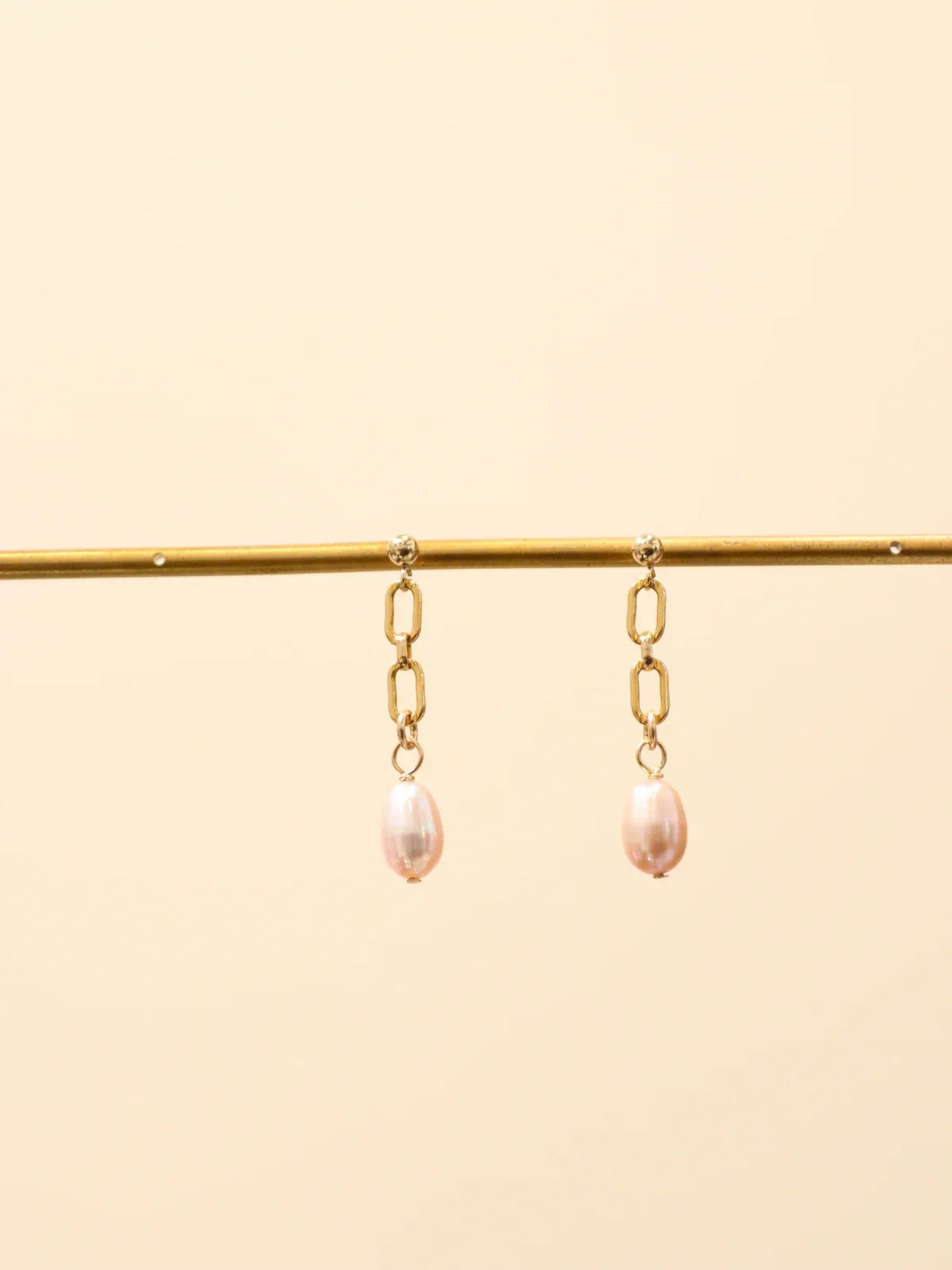 Pair of gold chain link drop earrings with oval white pearls, displayed on a jewellery stand
