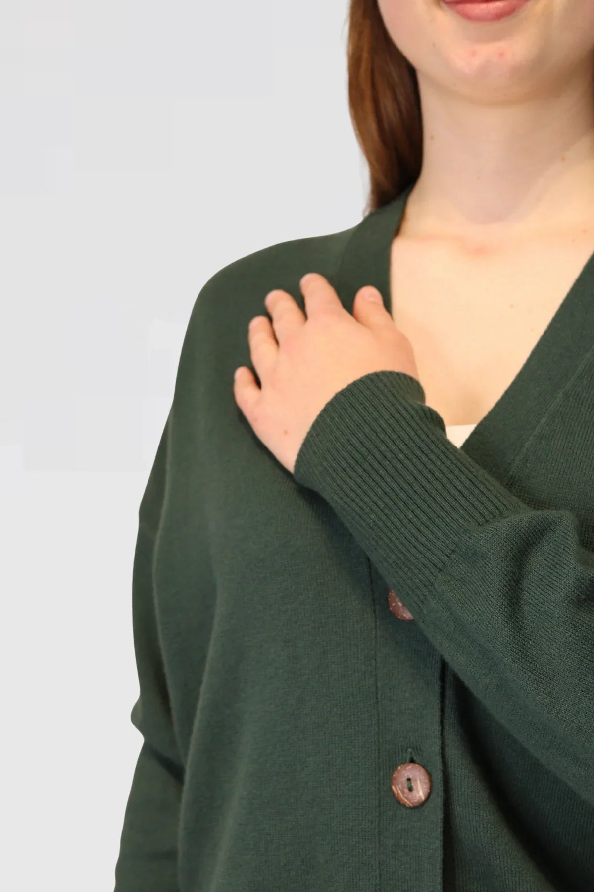 Person wearing a green cardigan with a plain background