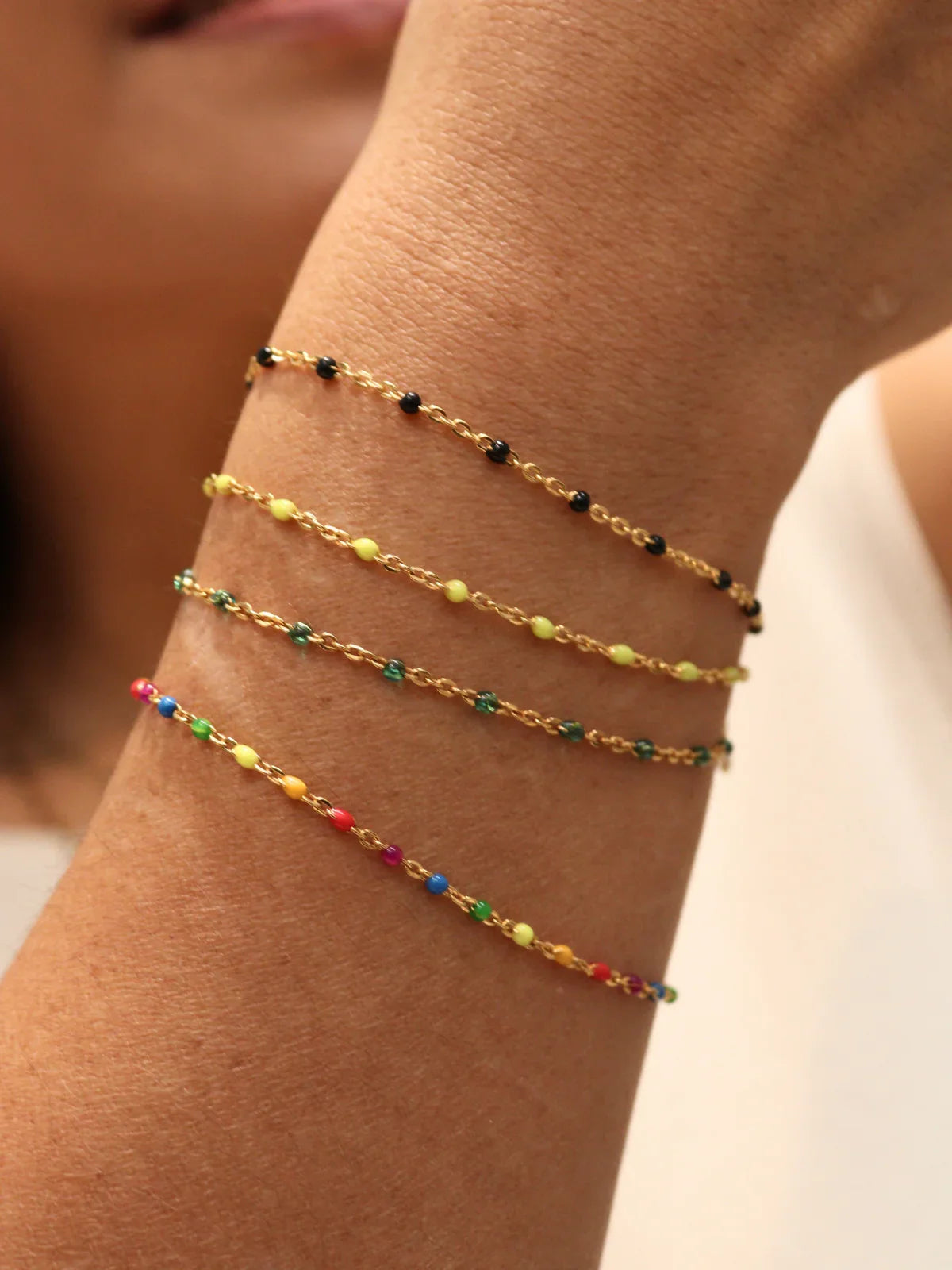 Close-up of a person's arm wearing two colorful beaded bracelets on a neutral background