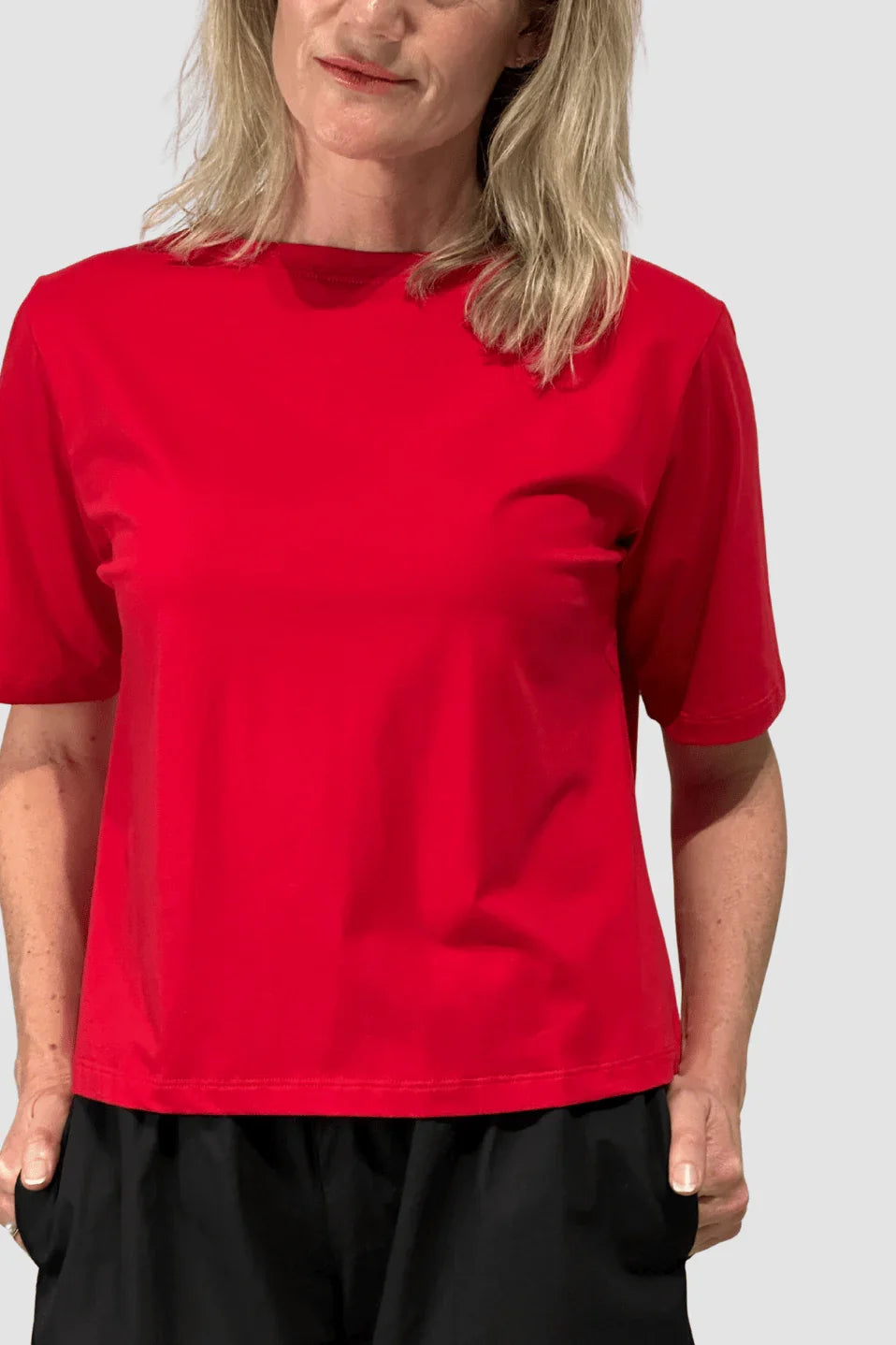 Woman wearing a bright red short-sleeve ethical cotton T-shirt paired with black pants on a plain background