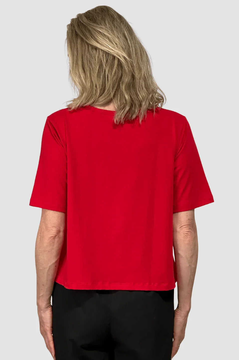 Rear view of a woman wearing a simple red short-sleeve ethical cotton t-shirt and black pants on a gray background