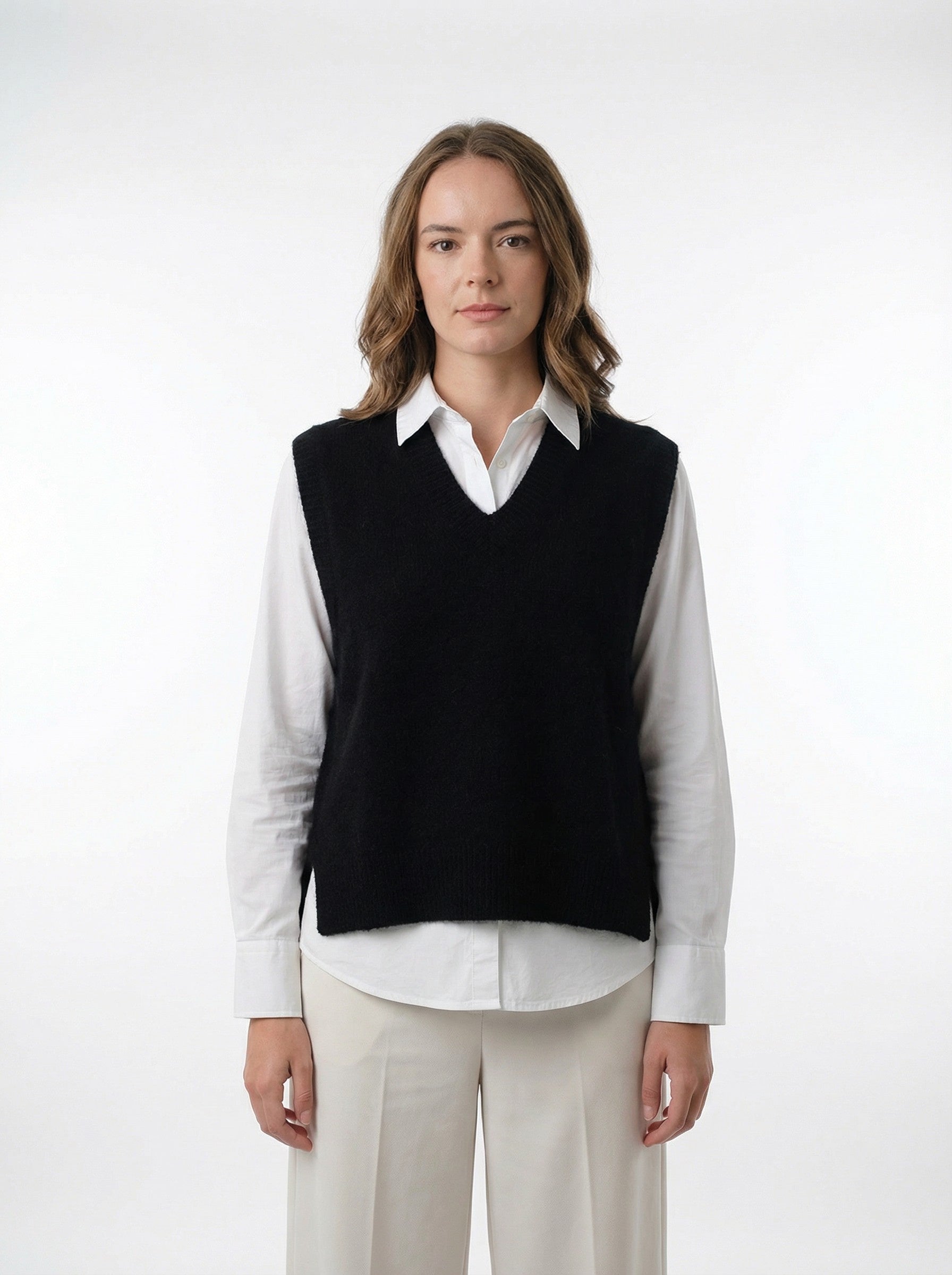 Woman in black knit vest over white shirt and cream wide-leg trousers, minimalist style