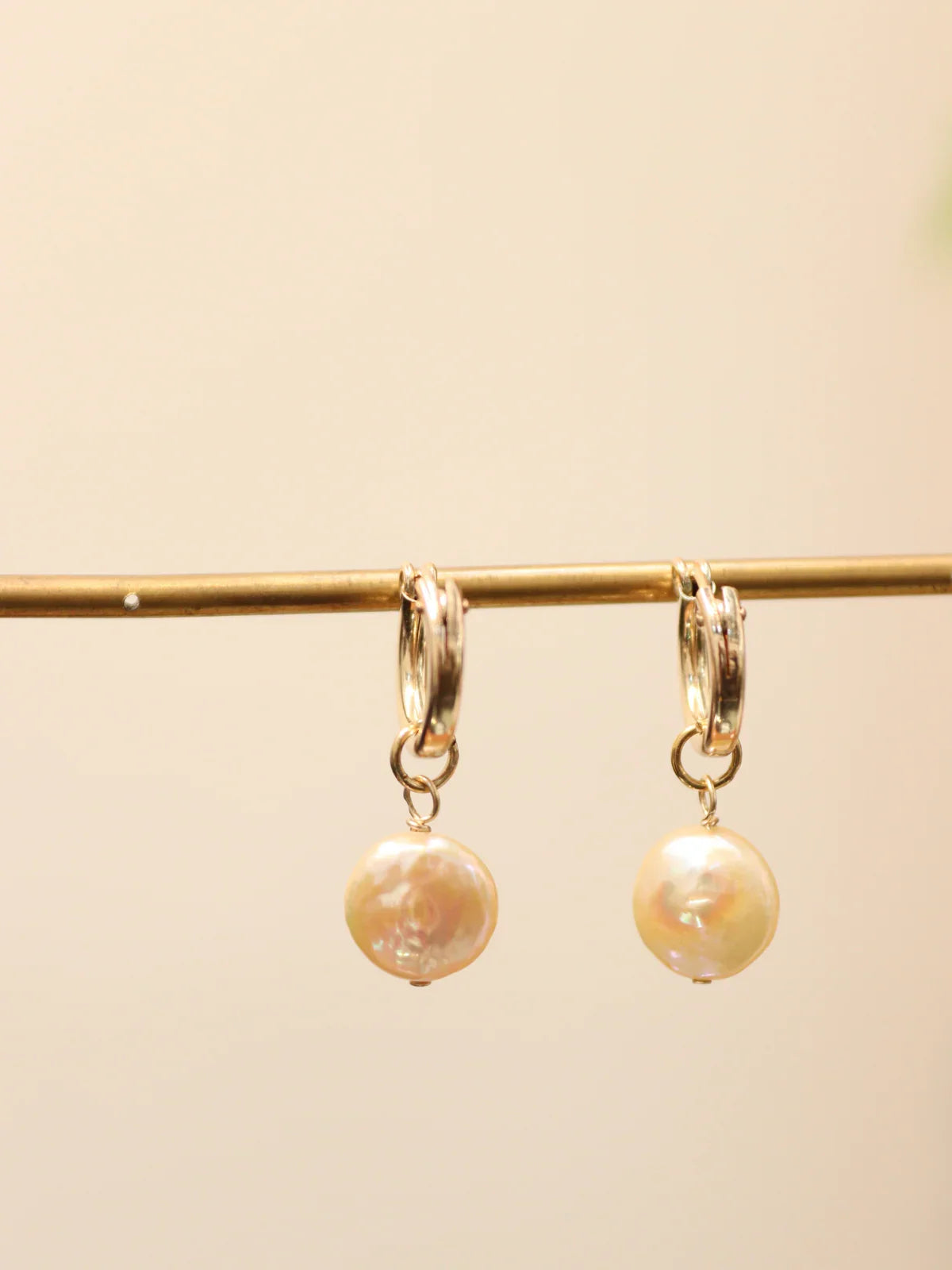 Pair of gold hoop earrings featuring coin pearls, displayed on jewellery stand.