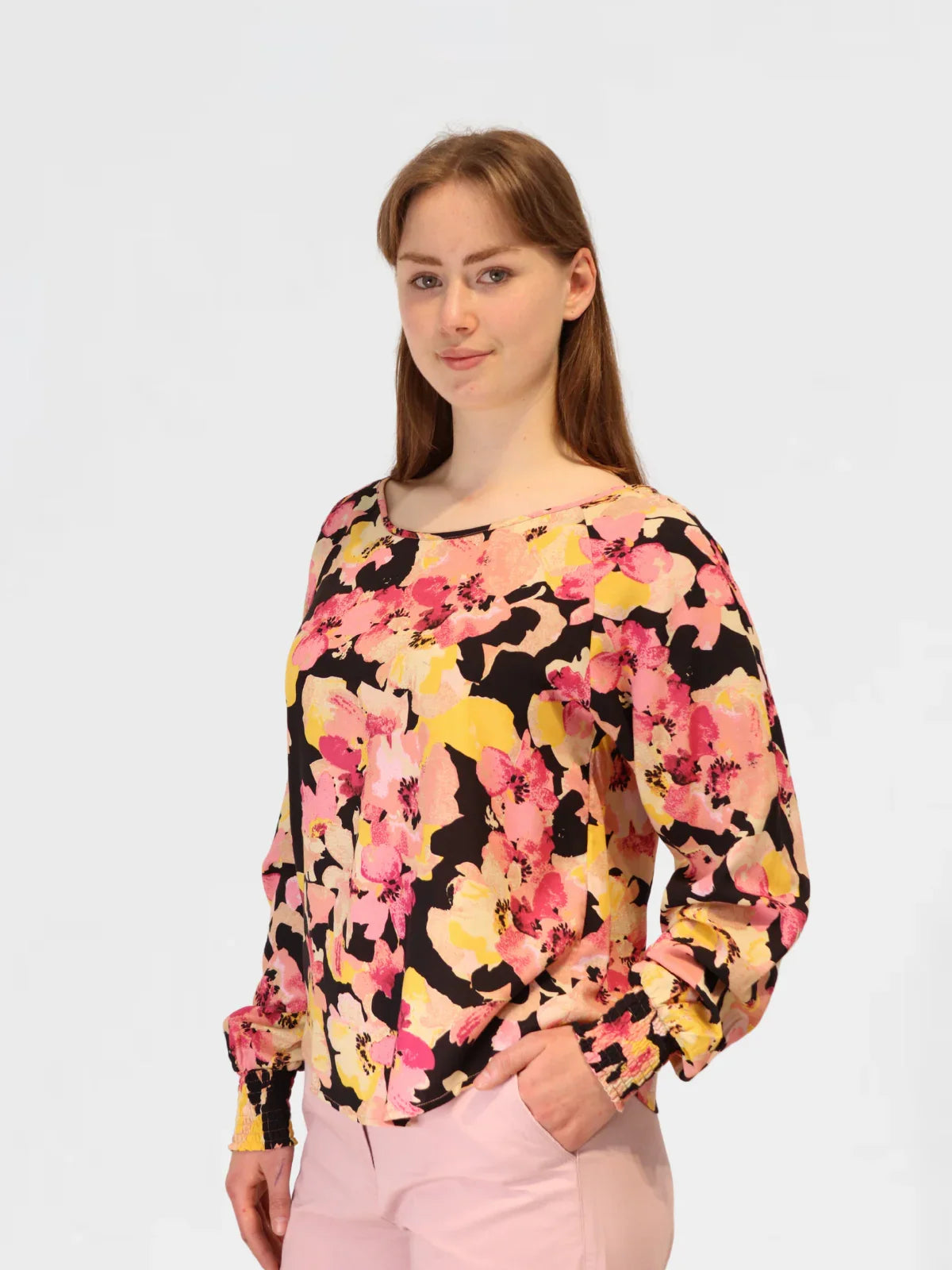 Woman modelling vibrant floral blouse with gathered sleeves and bold flower print, paired with pink pants.