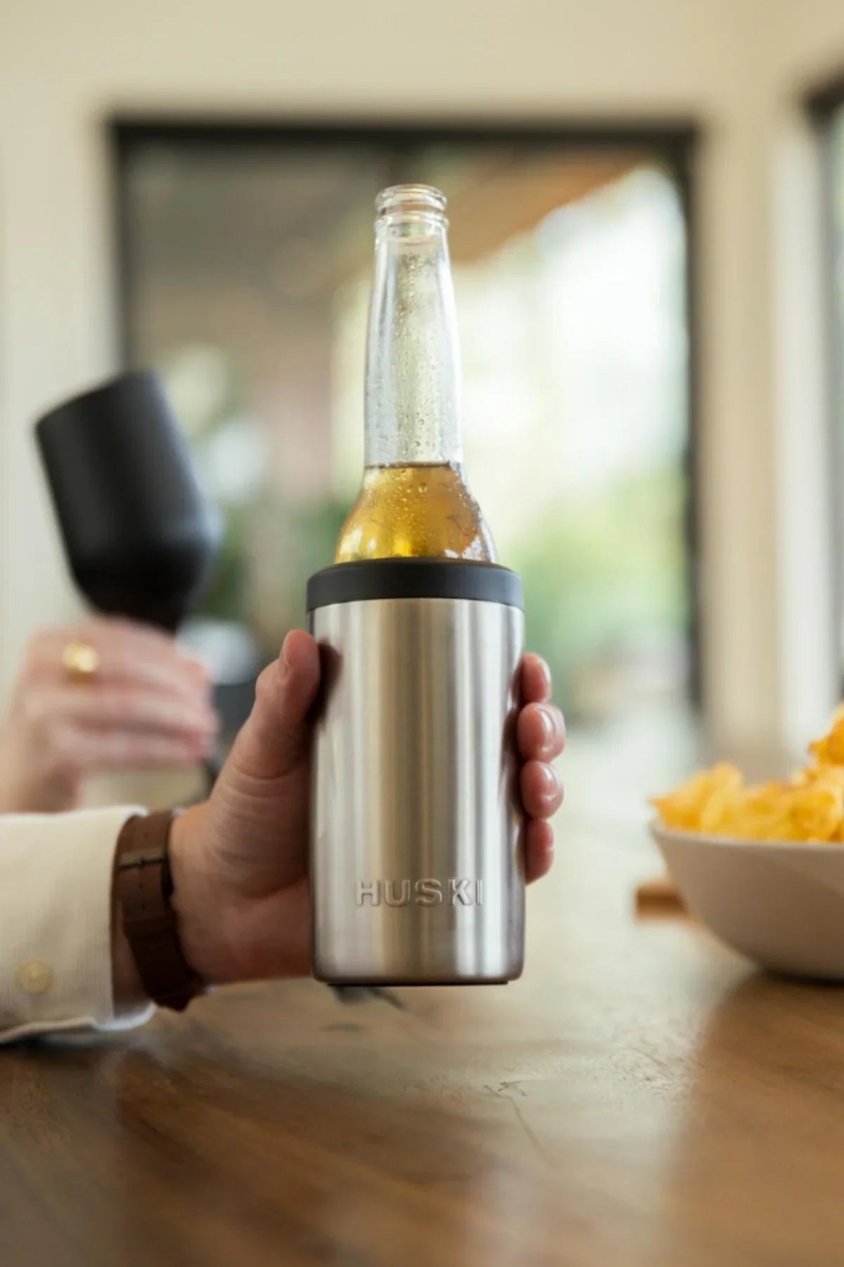 Person holding a Huski insulated bottle with a beer bottle inside, blurred background