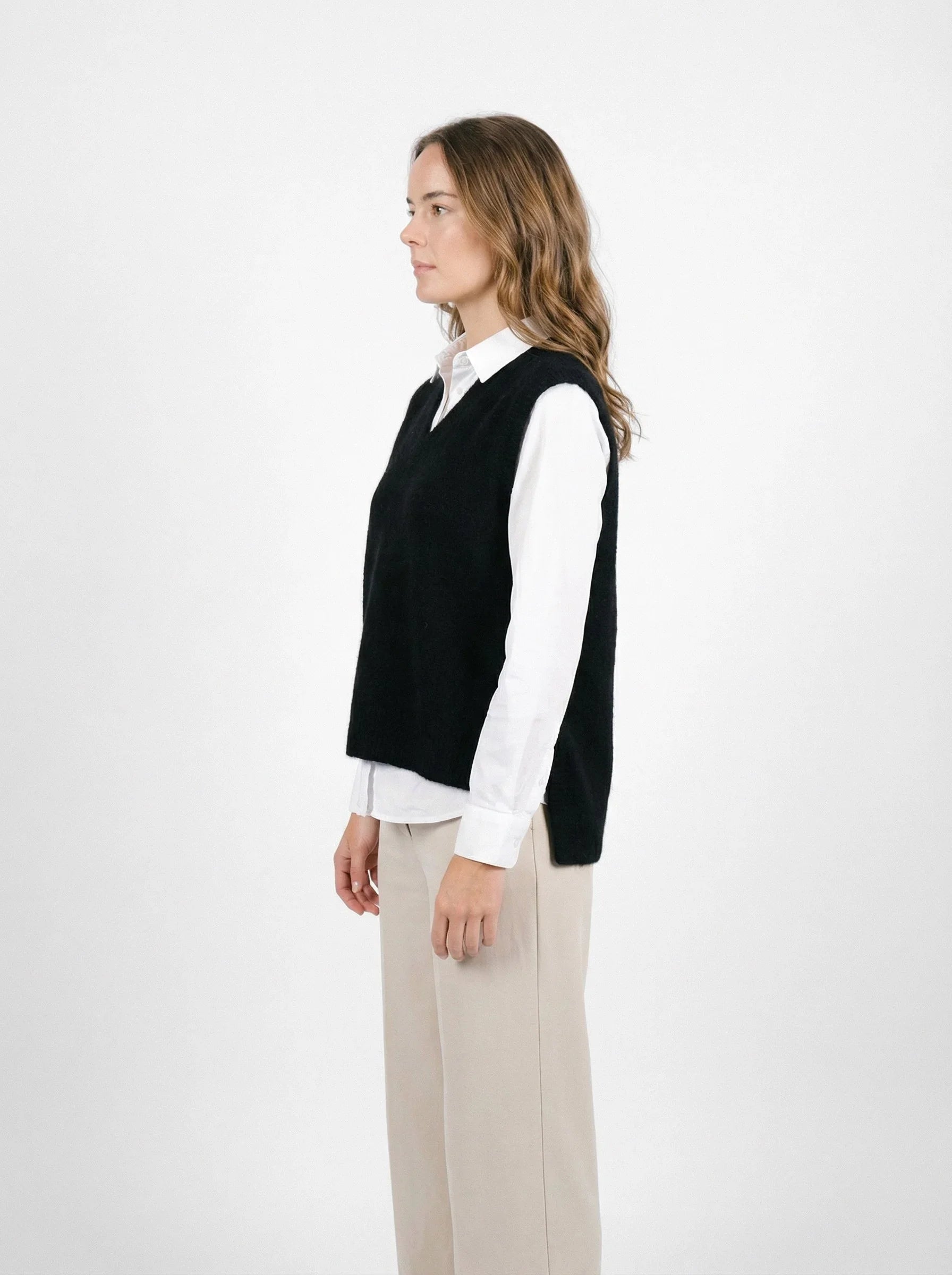 Woman wearingPossum Merino Ride Vest - Black over white shirt and beige trousers, side view