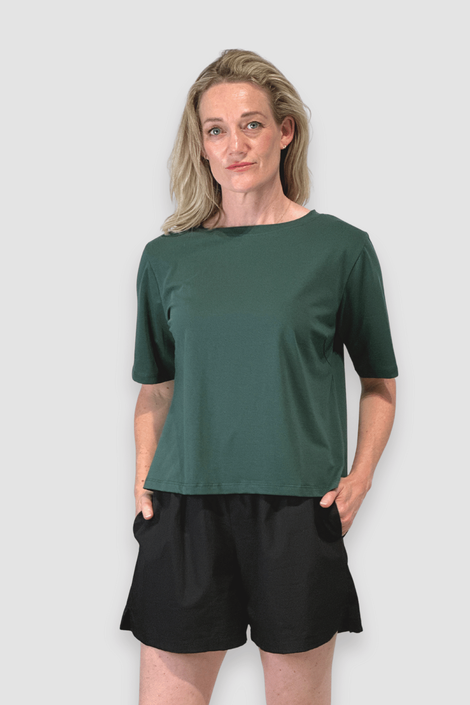 Woman in green short-sleeve top and black shorts posing against plain background