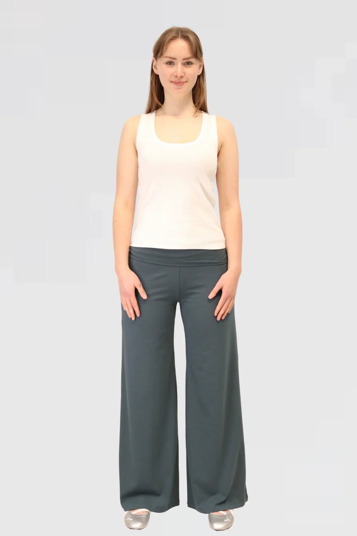 Woman wearing a white tank top and blue yoga pants on a light grey background