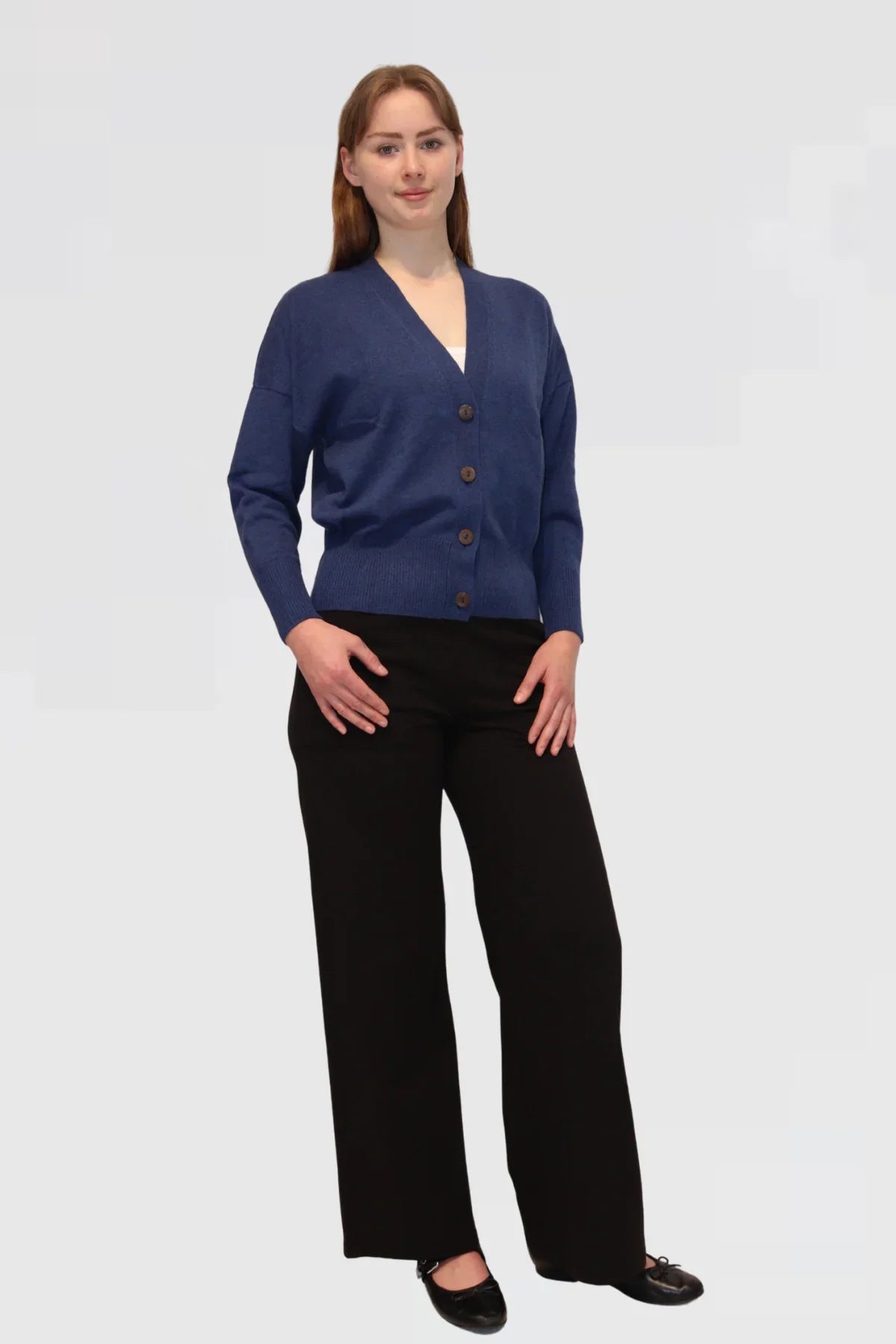 Woman wearing a blue cardigan and black pants on a white background