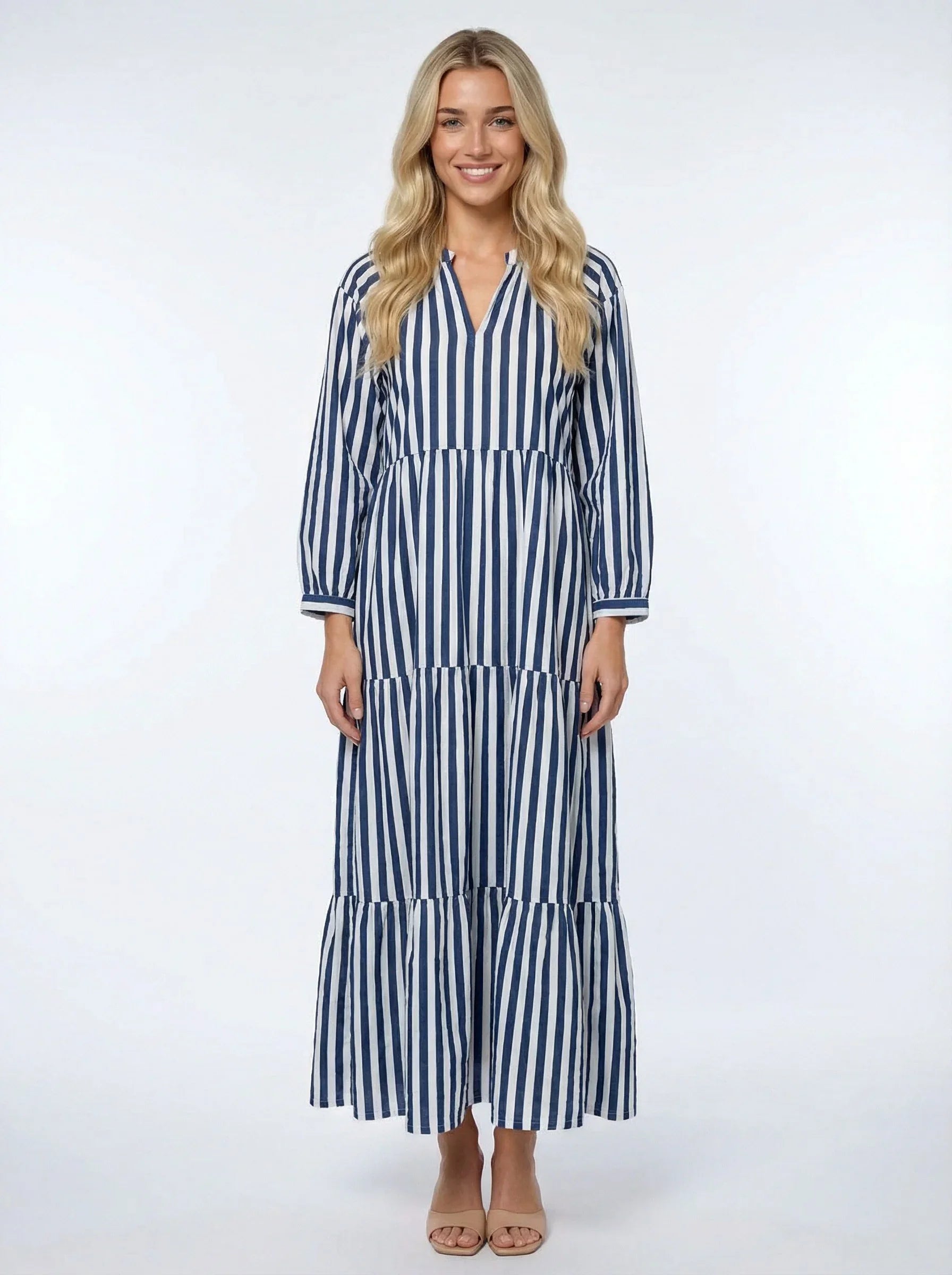 Smiling woman wearing blue and white striped long sleeve maxi dress on plain white background