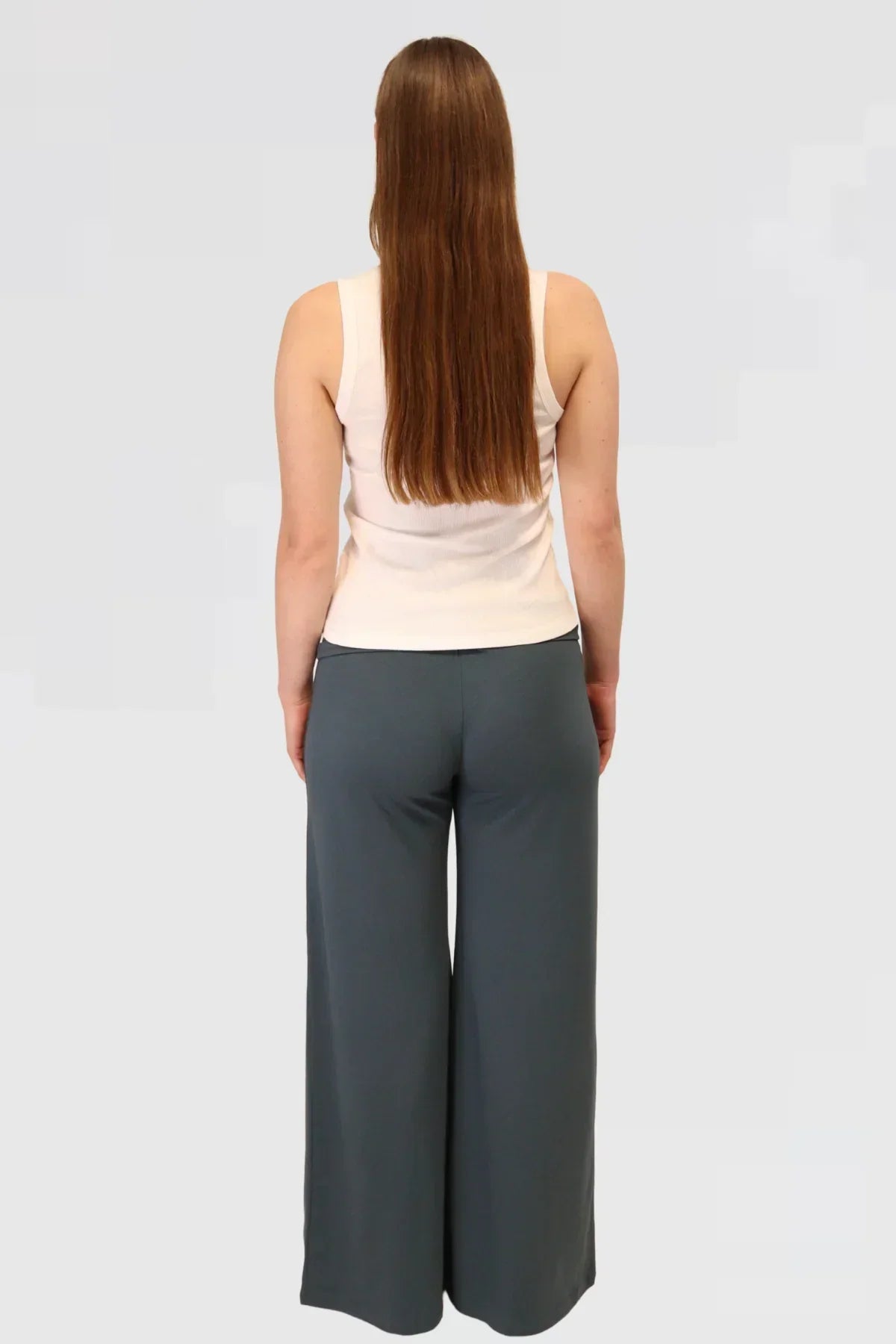 Person wearing a white tank top and blue yoga pants on a light grey background