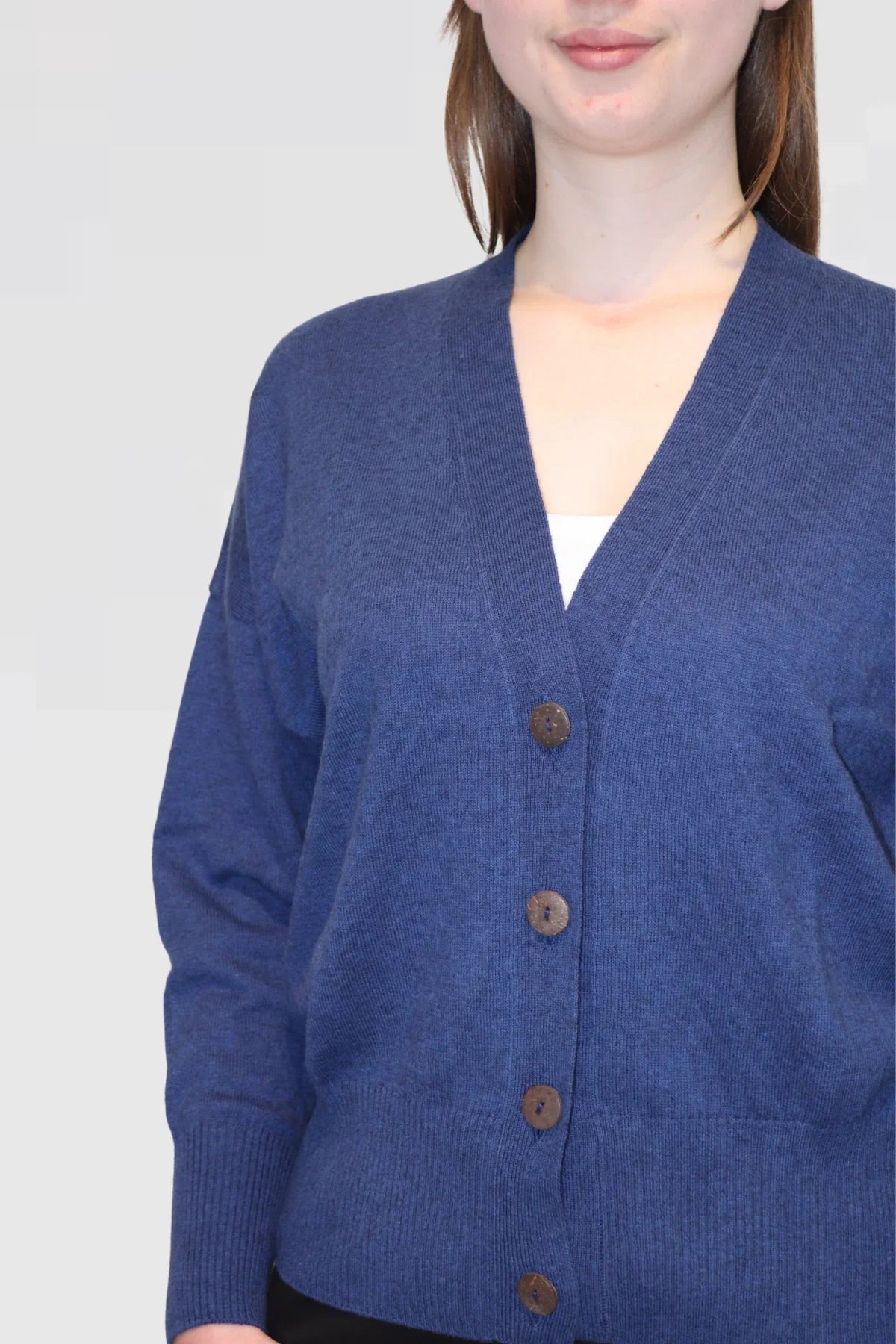 Person wearing a blue cardigan with brown buttons on a plain background