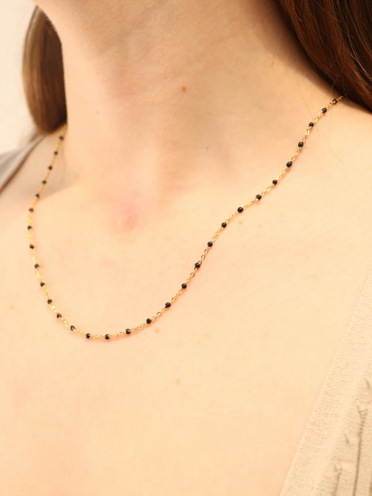 Gold chain necklace with evenly spaced black beads, worn on neck.