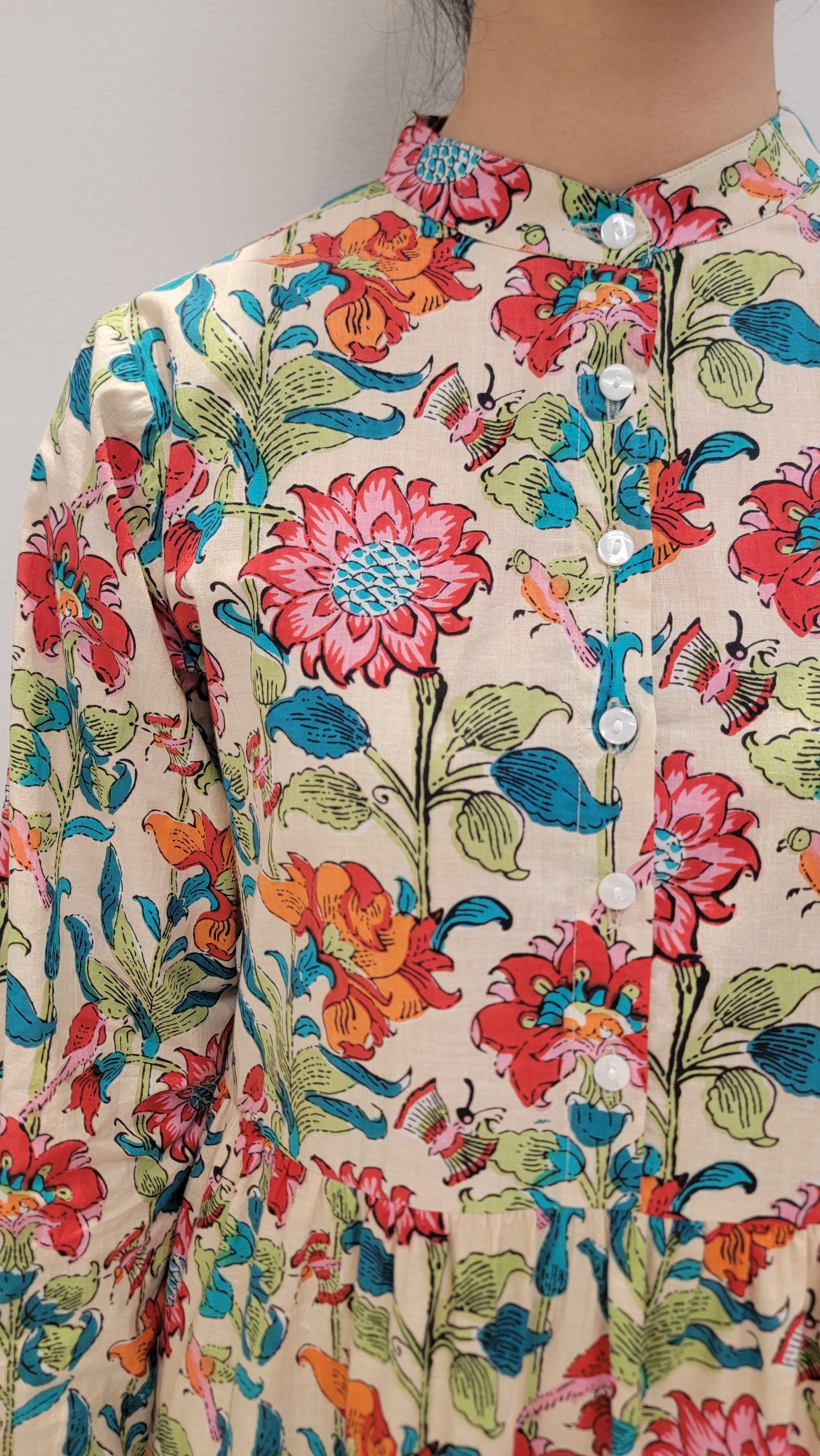 Close-up of a Bloomfield Garden Dress with colorful flowers on a beige background