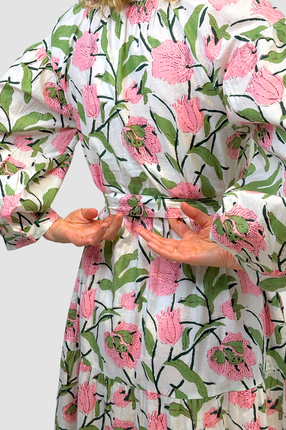 Person wearing a floral patterned dress with pink flowers and green leaves on a white background