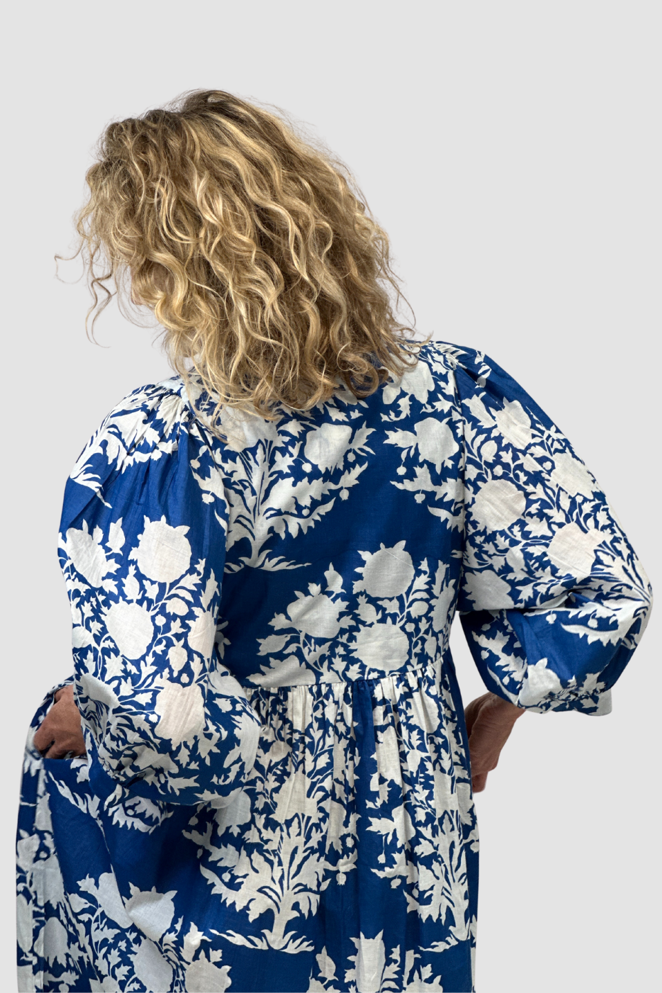 Woman wearing a blue and white floral dress against a plain background
