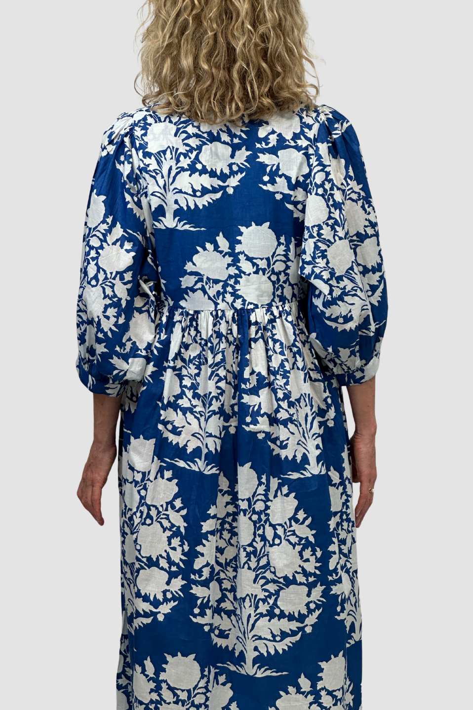 Woman wearing a blue and white floral dress against a plain background