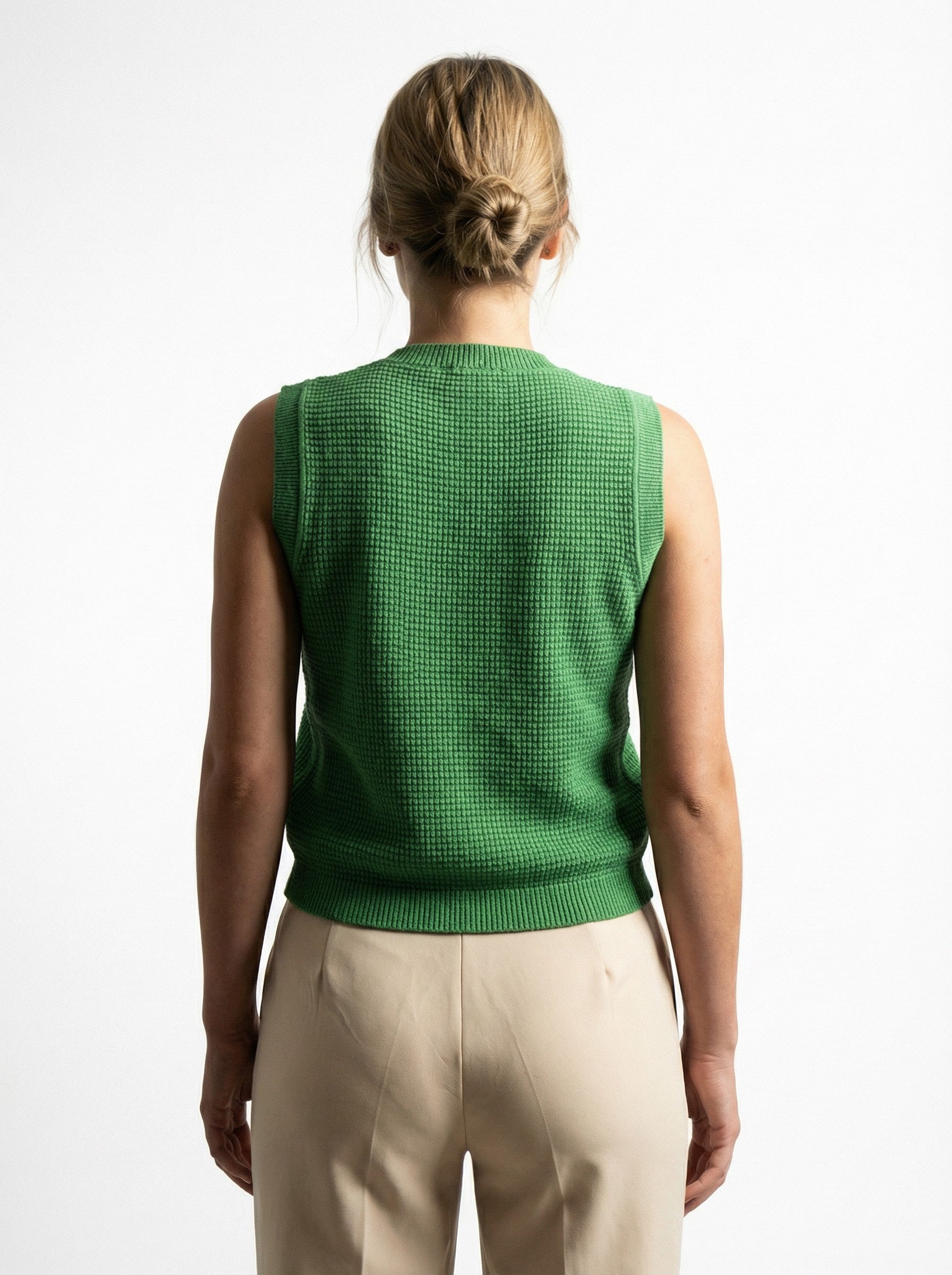 Person wearing a COTTON & MERINO HEPBURN BUTTON VEST - KELLY GREEN and beige pants on a white background