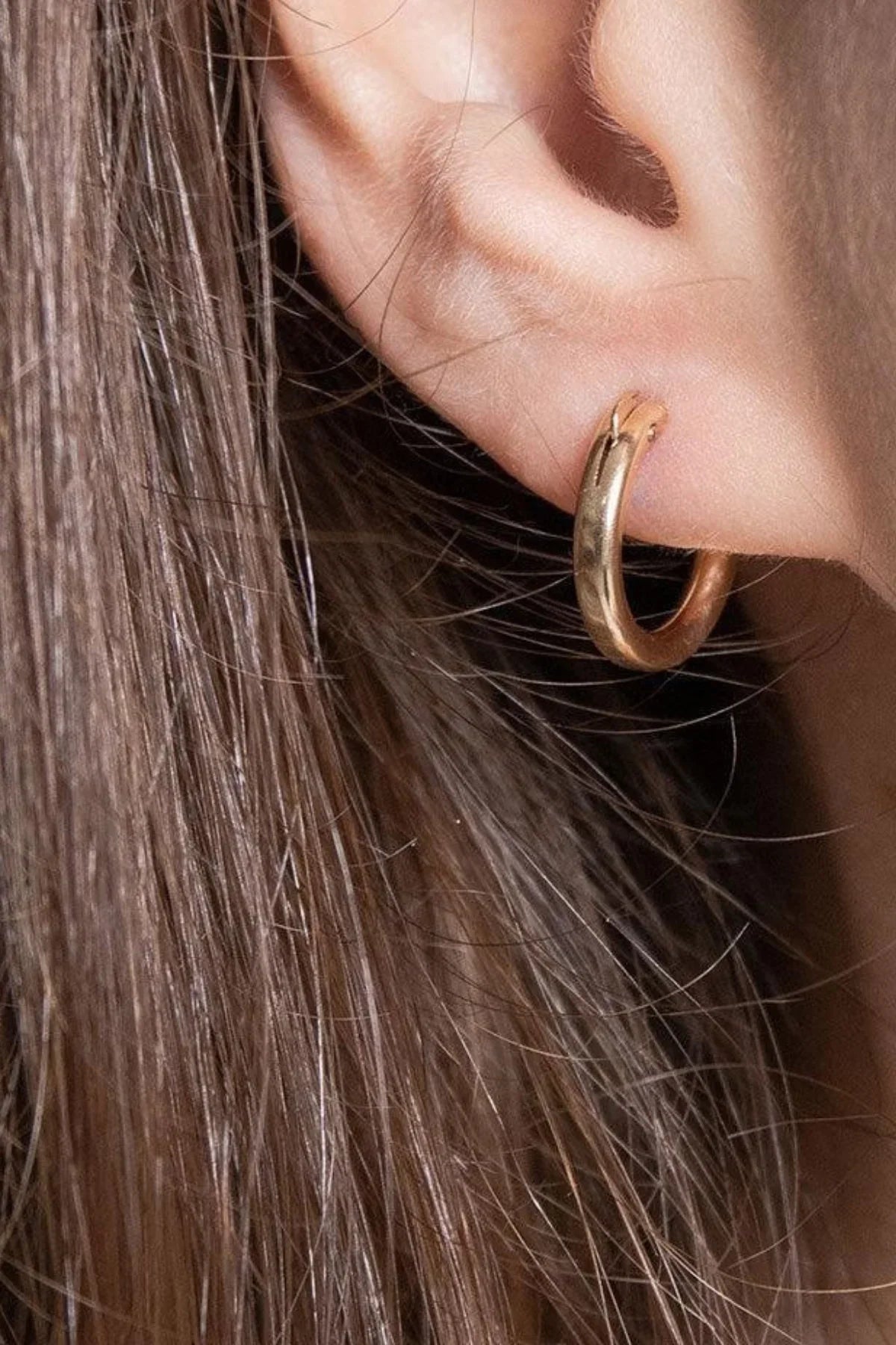 Close-up of small gold hoop earring worn on ear.