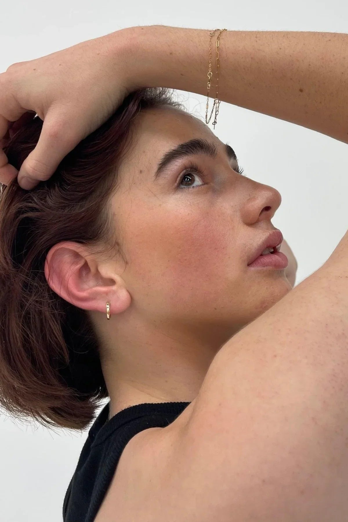Woman wearing small gold hoop earrings with matching bracelet.