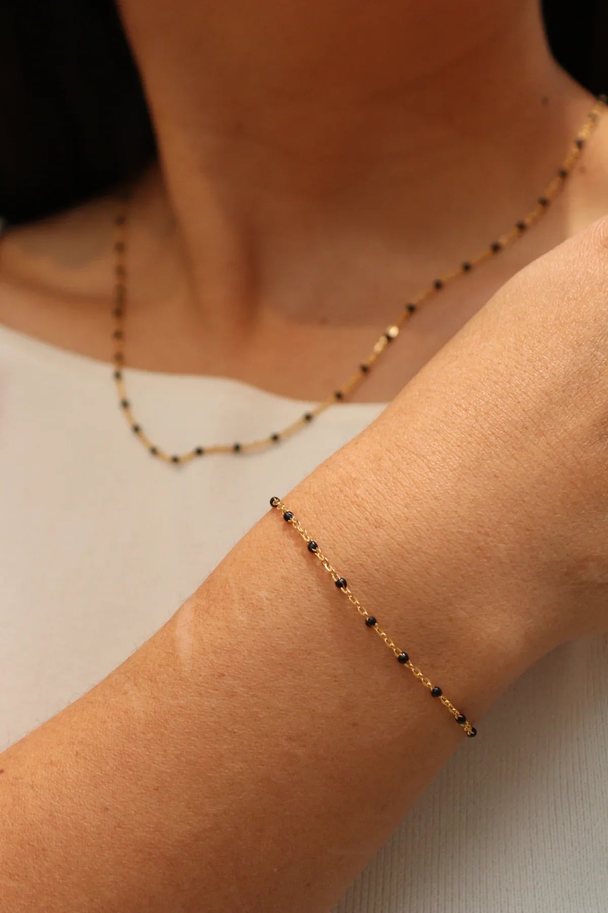 Close-up of a person wearing a delicate gold bracelet with black beads on a plain background