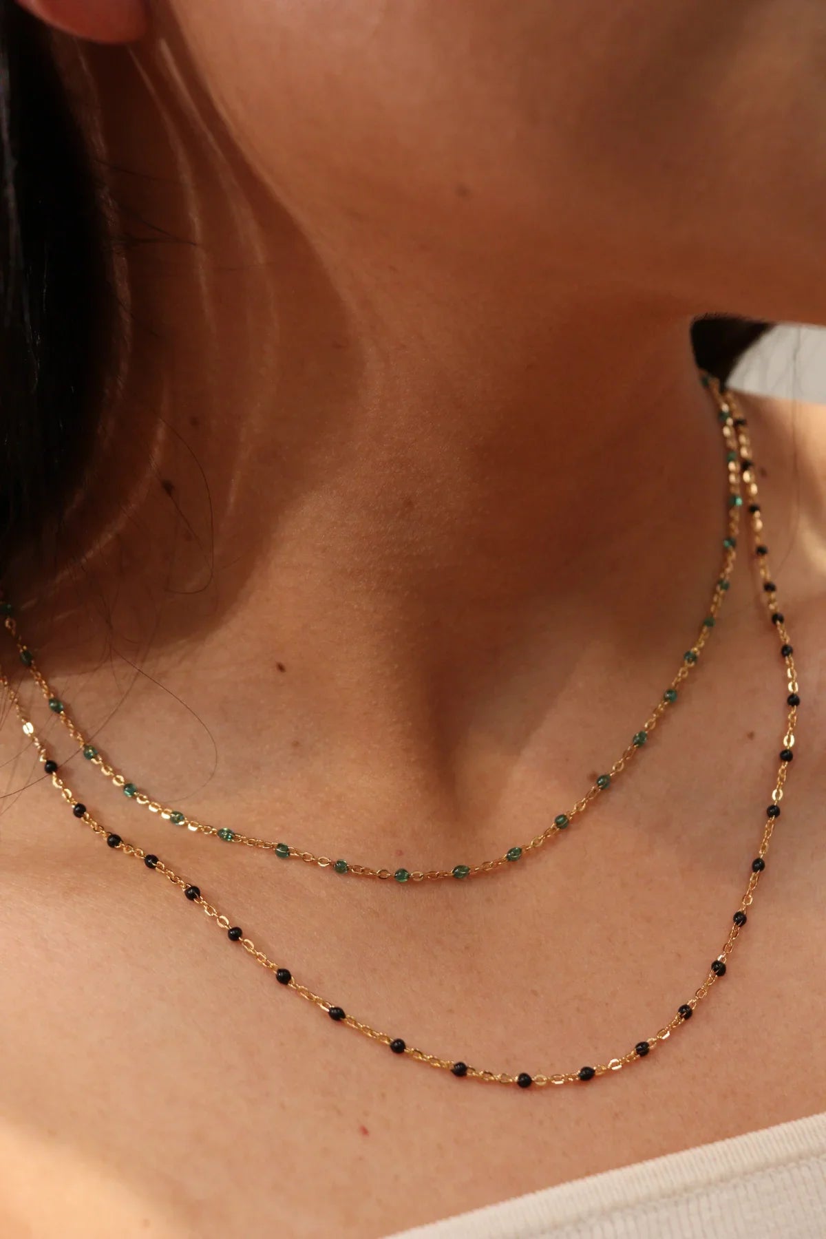 Close-up of a person wearing two gold necklaces with green beads.