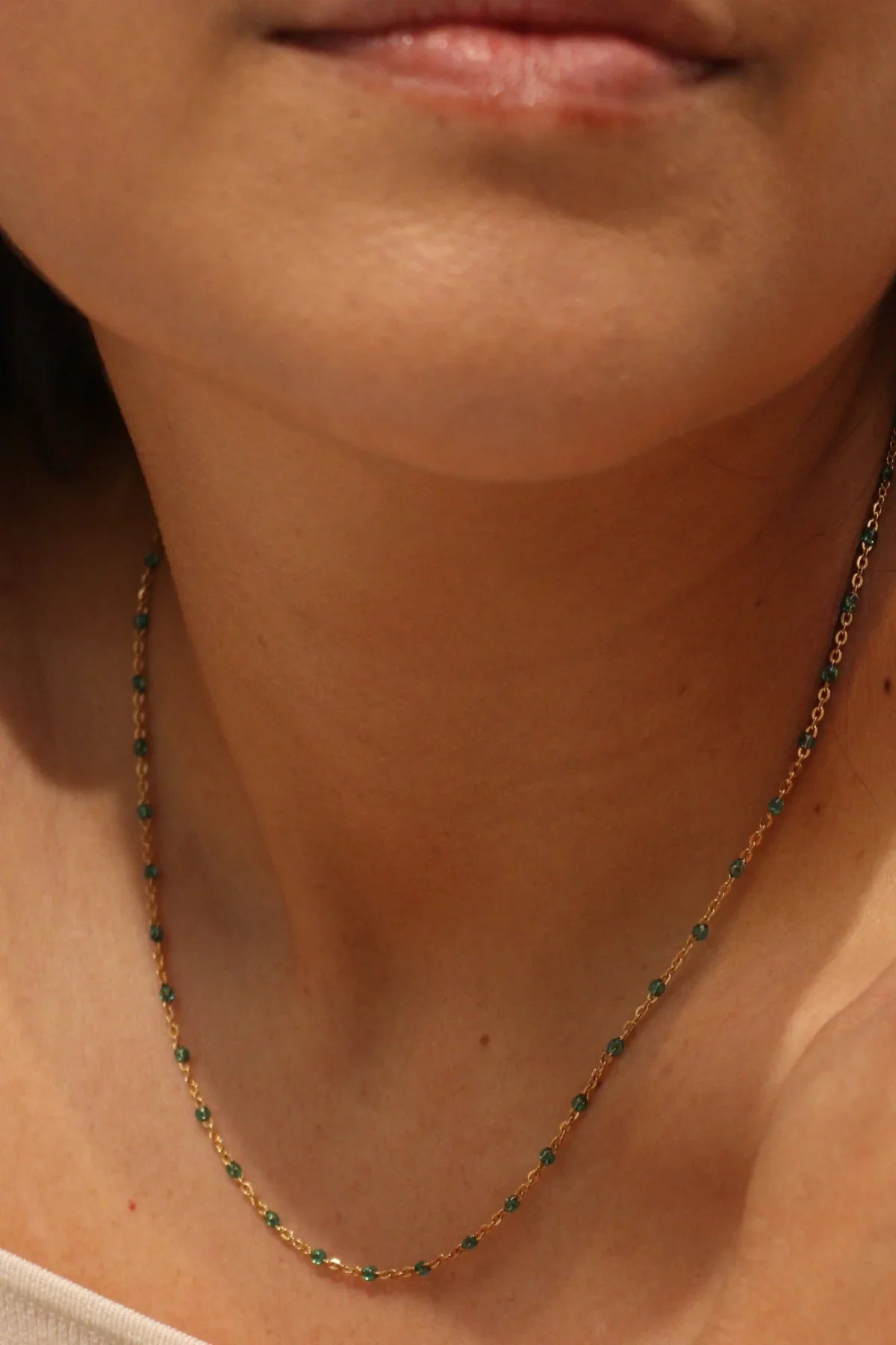 Close-up of a person wearing a gold necklace with green gemstones.