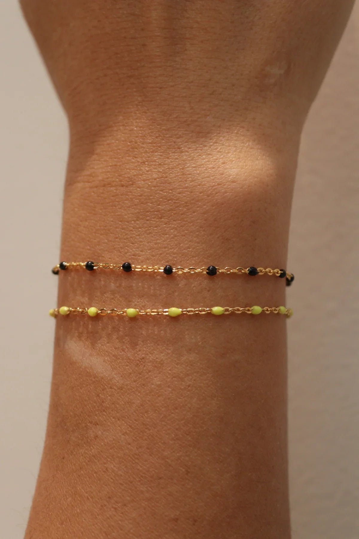 Gold bracelet with black and yellow beads on a wrist against a beige background