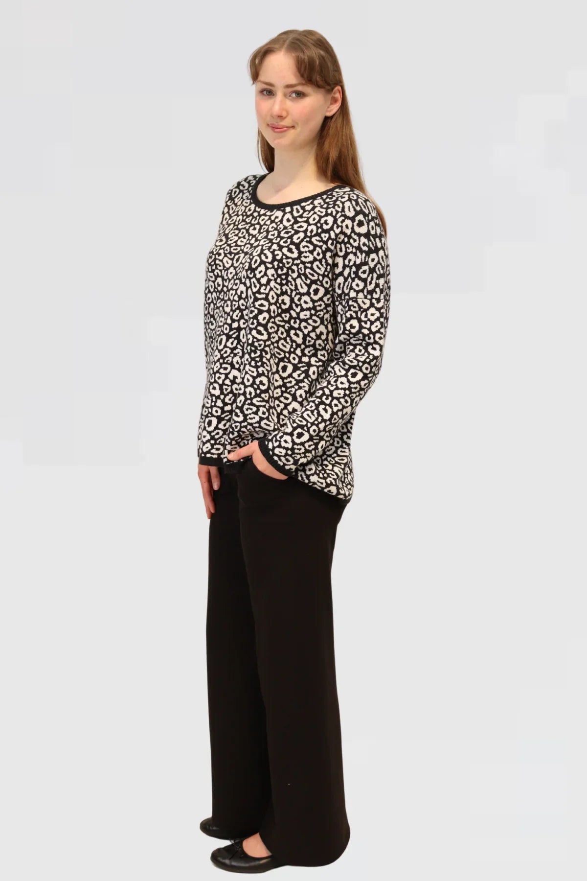 Woman showcasing side of the black and white patterned top with black pants on a white background