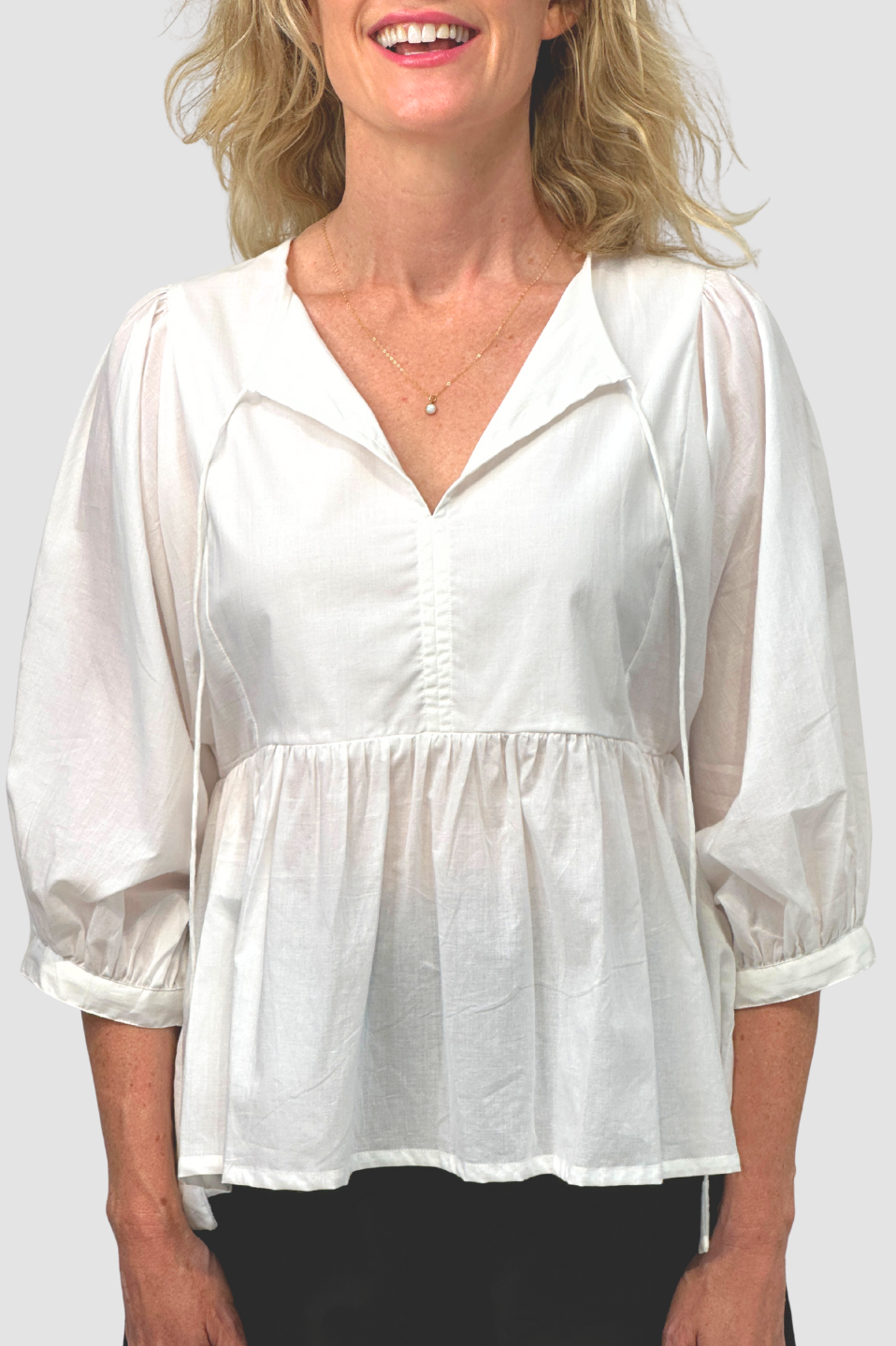 Woman wearing white loose-fit blouse with balloon sleeves and V-neck, smiling