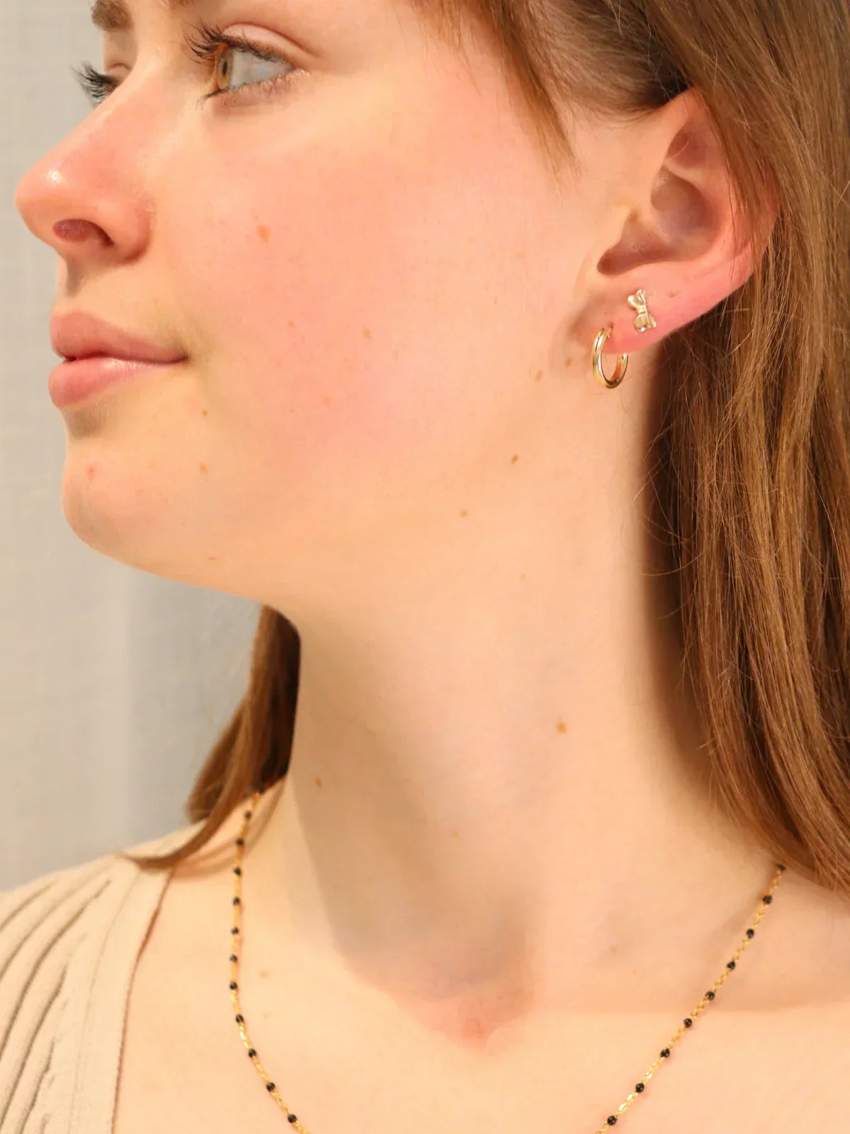 Woman wearing gold bow stud earrings with matching hoop.