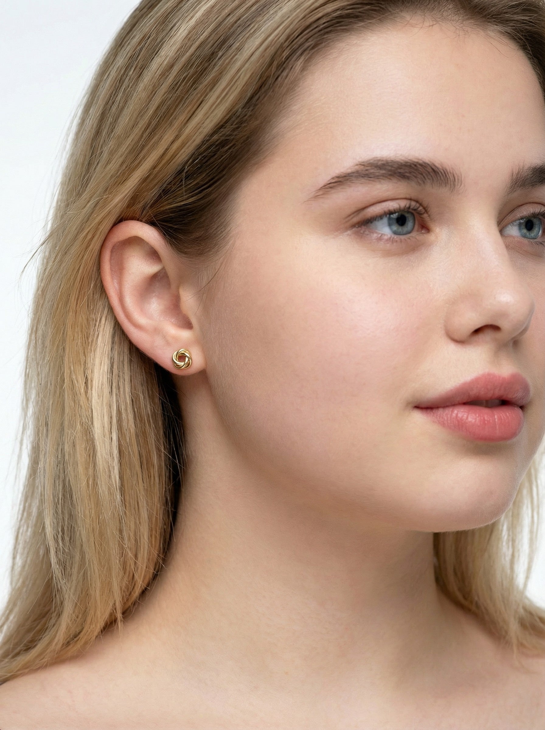 Close-up of a woman wearing a gold knot earring with a plain background