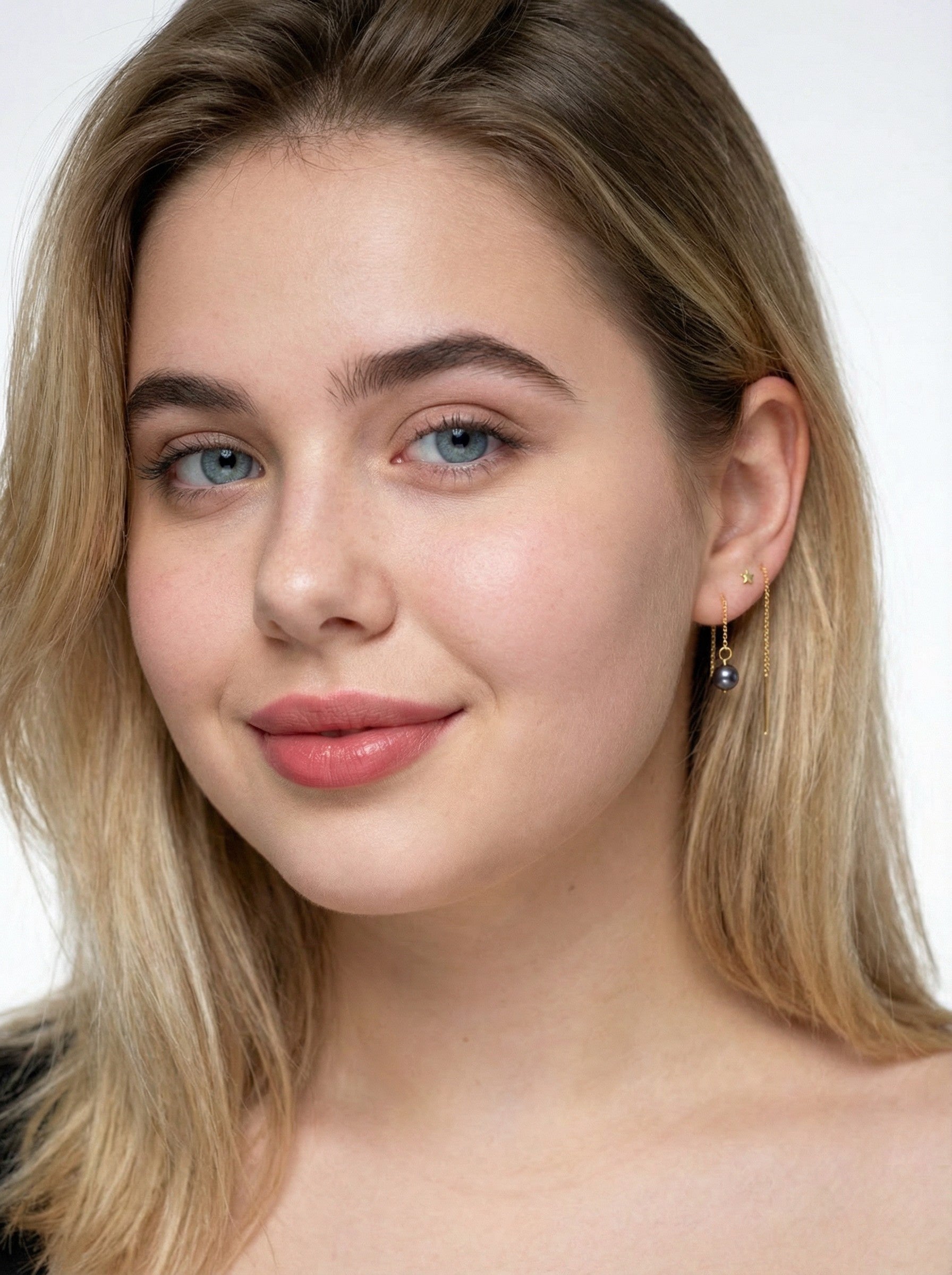 Woman with blonde hair and blue eyes wearing earrings from Reca called Gold Noir Pearl Threader Earrings on a white background