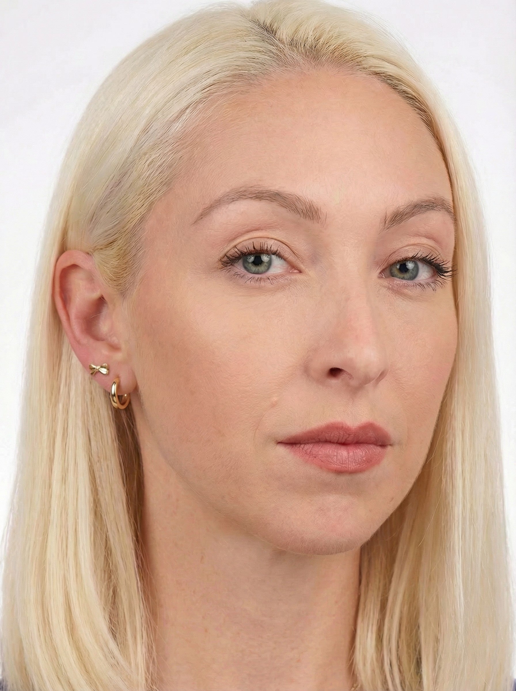 Close-up of a woman with blonde hair and blue eyes wearing Gold Sleeper Earrings on a white background