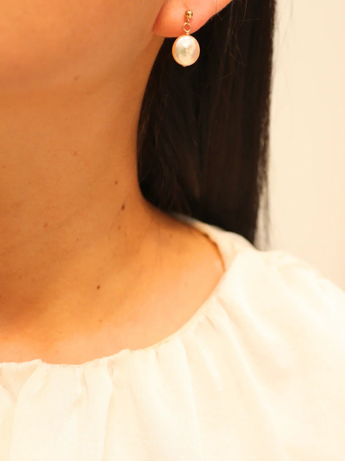 Gold drop earring with single round pearl, worn on ear.