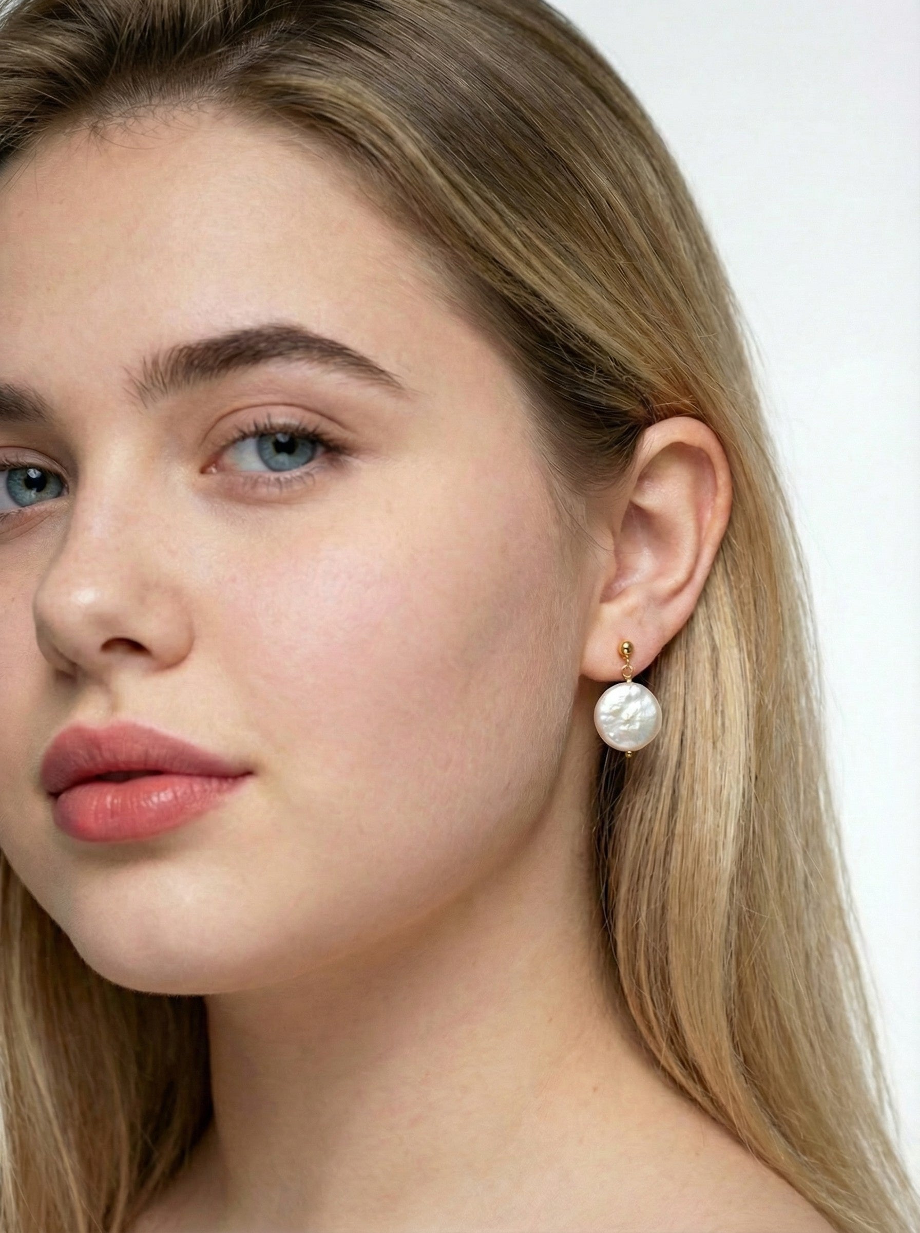 Close-up of a woman wearing Golden Halo Pearl Earrings with a plain background