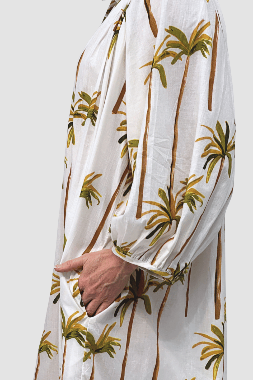 White dress with palm tree pattern held by a hand against a white background