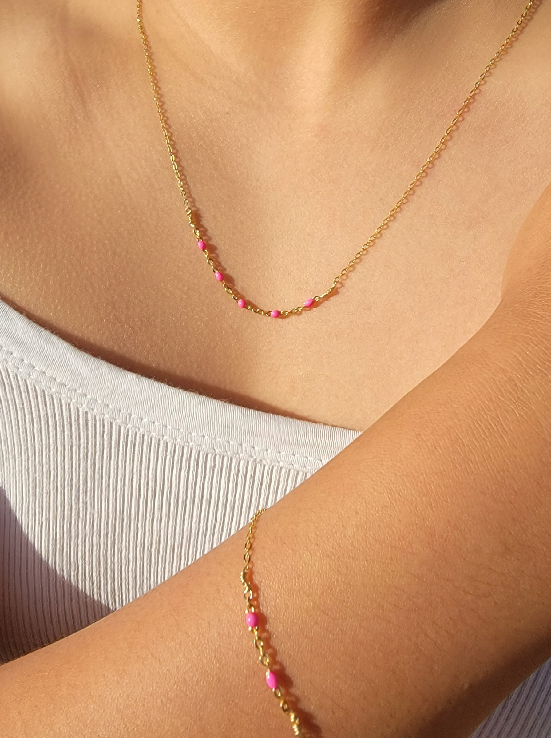 Close-up of a Hot Pink Enamel Satellite Necklace and matching bracelet on a person wearing a white top
