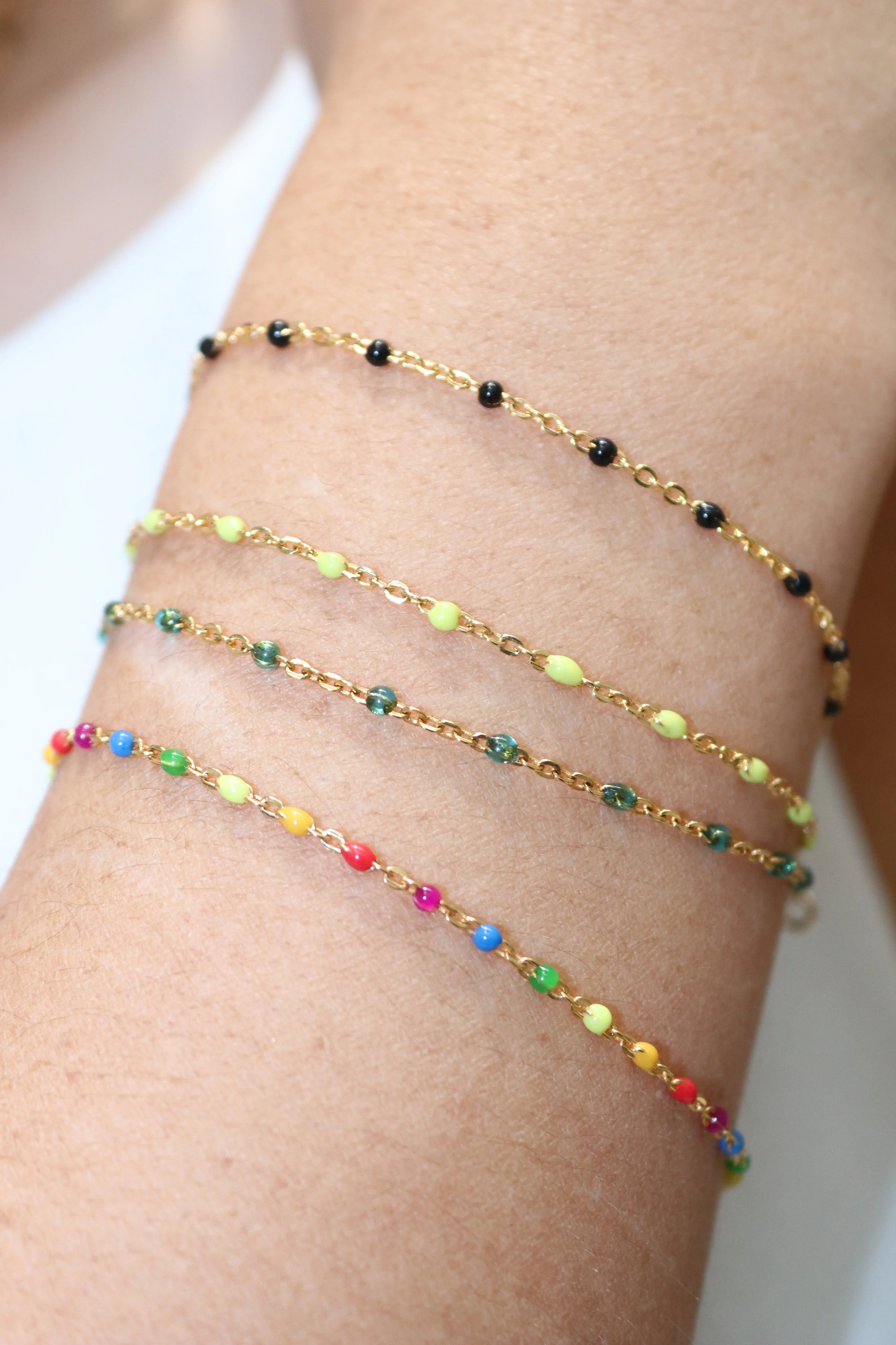 Three gold beaded bracelets on a wrist with multicolored beads.