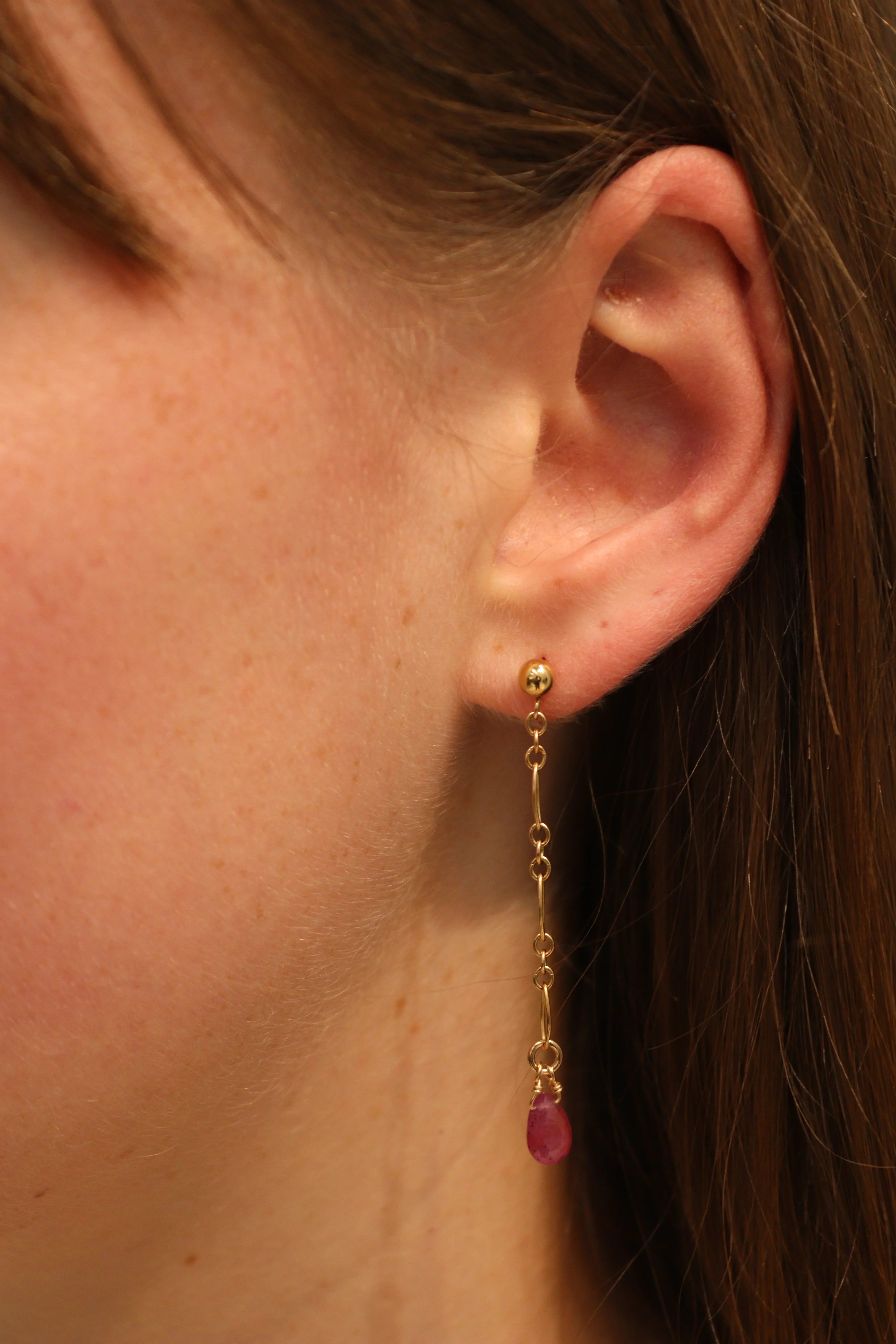 Close-up of an ear with a gold earring featuring a red gemstone.