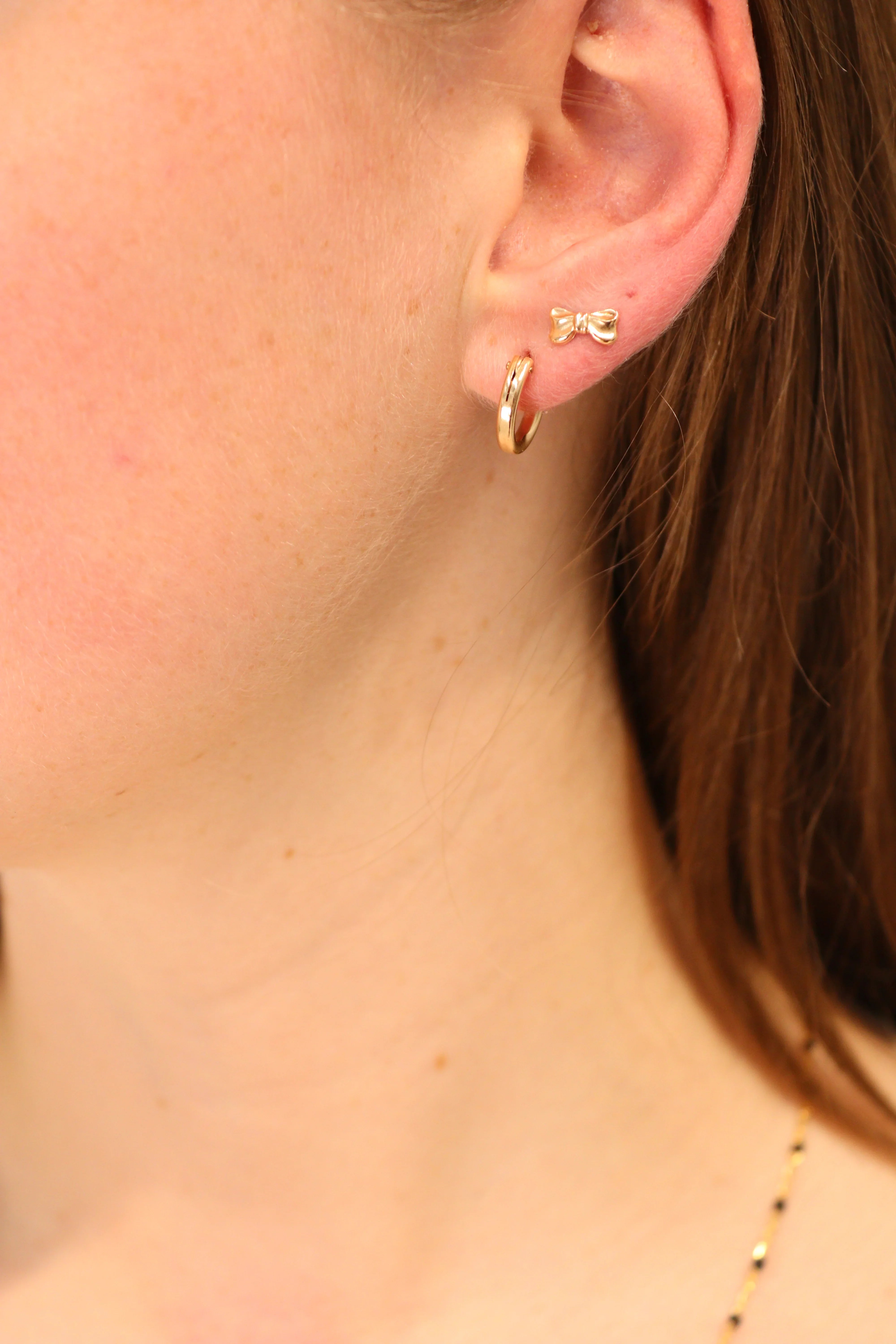 Gold bow stud and hoop earrings styled together on ear.