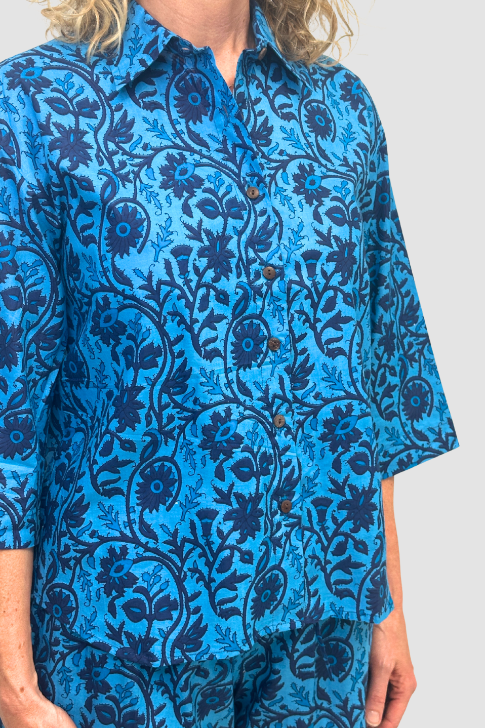 Blue button-up shirt with dark floral and vine pattern, Named the "Indigo Tide Button Down" worn with matching pants