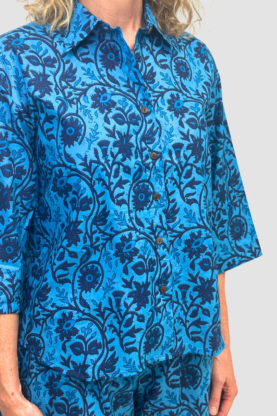 Blue button-up shirt with dark floral and vine pattern, Named the "Indigo Tide Button Down" worn with matching pants