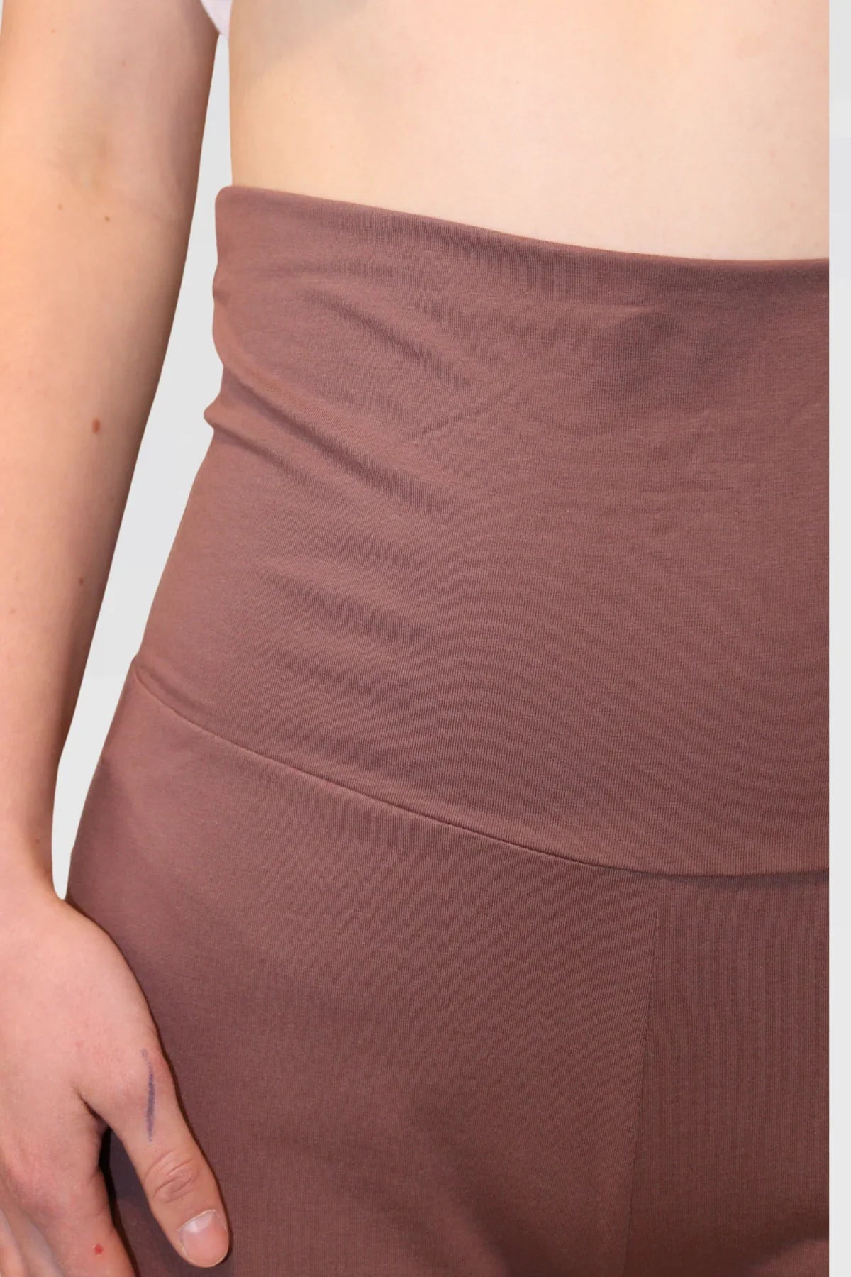 Woman wearing a white tank top and Leisure Lux Pants - Mocha Mousse on a light gray background - close up front