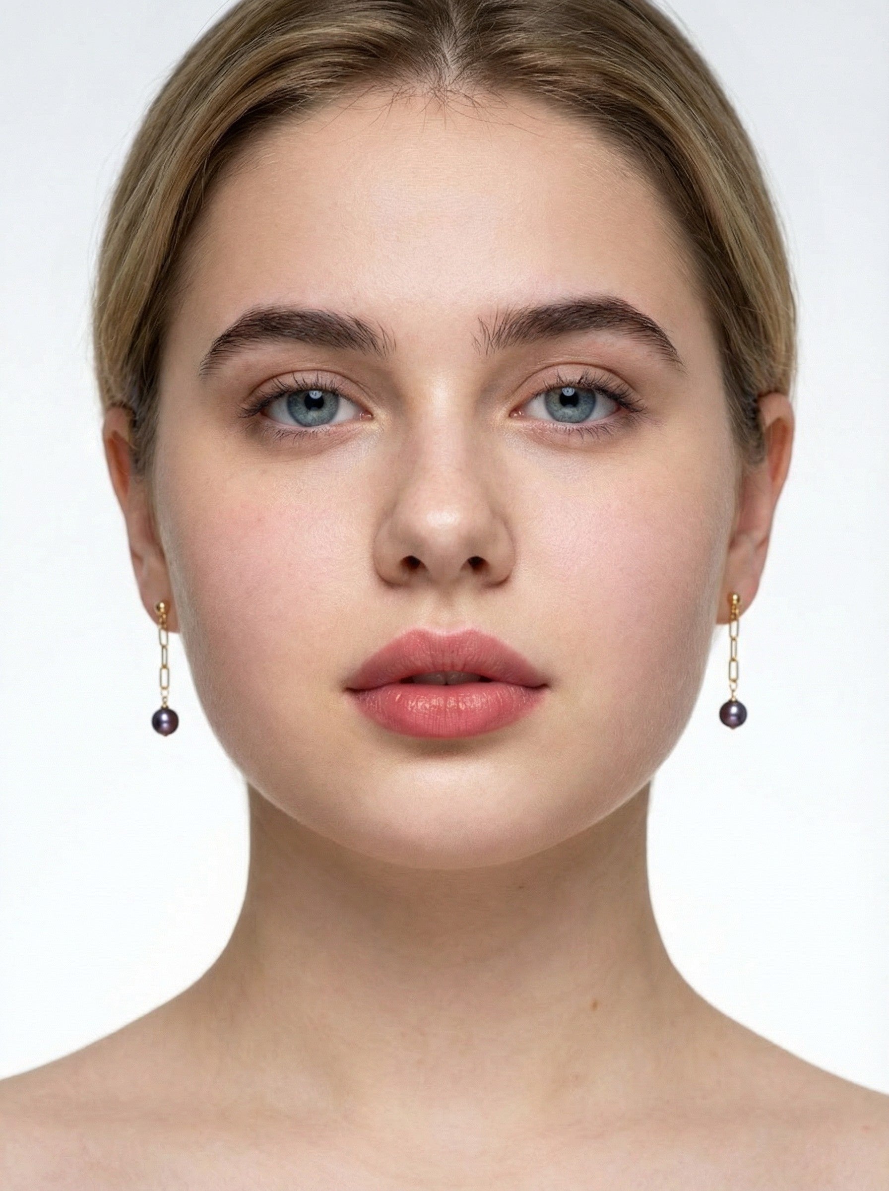 Close-up of a person wearing gold purple pear earrings with dark beads on a white background