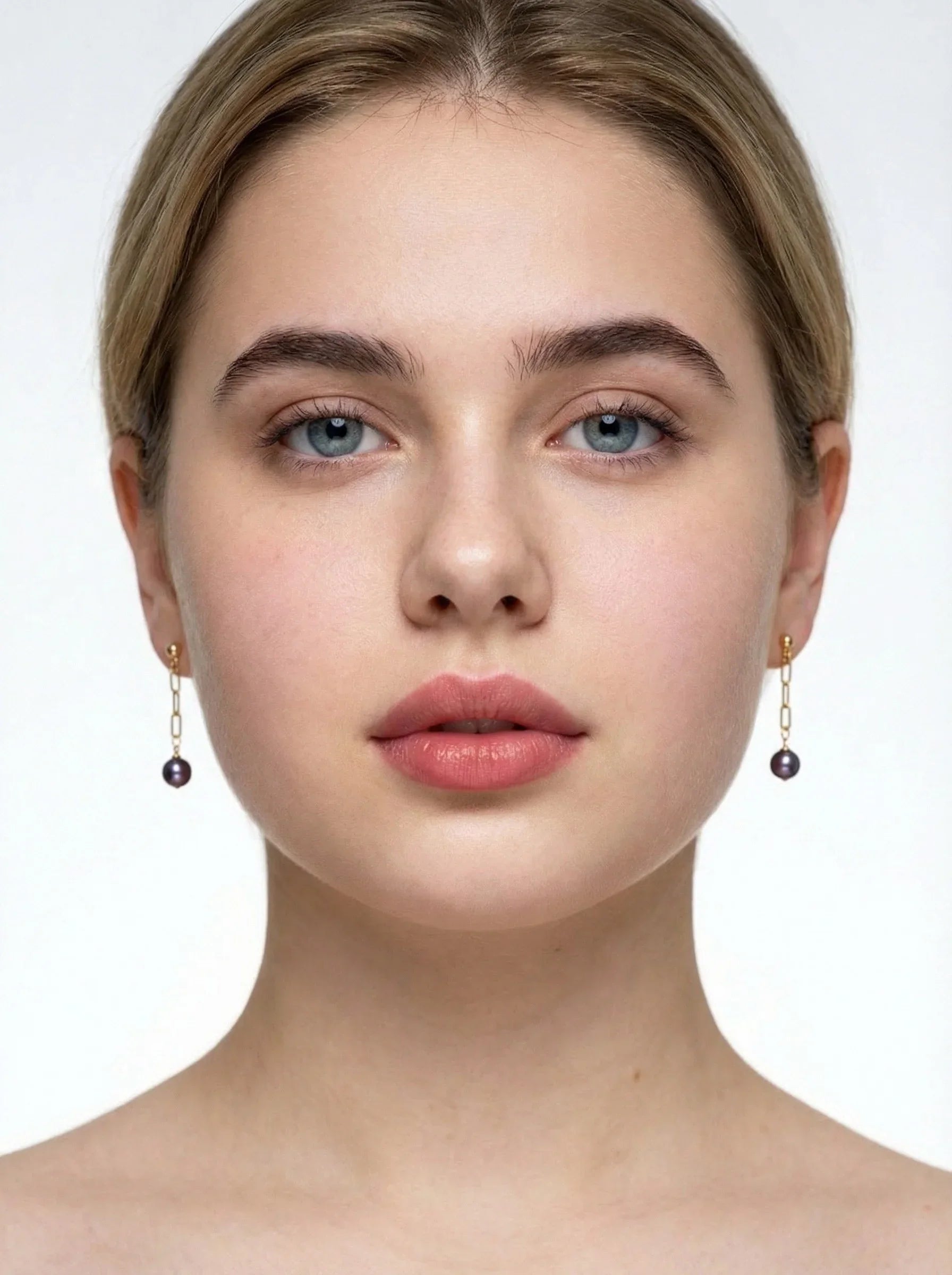 Close-up of a person wearing gold purple pear earrings with dark beads on a white background