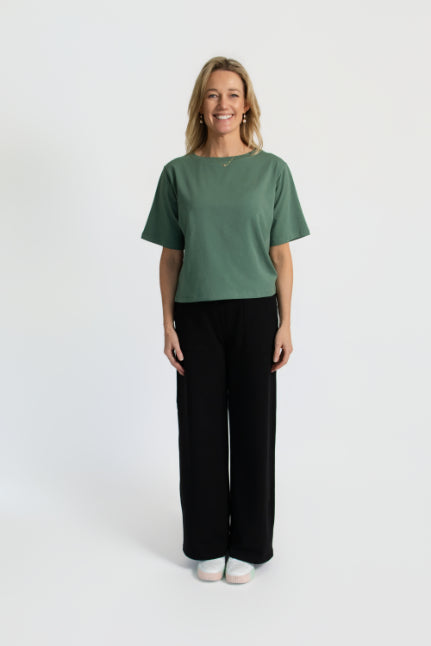Model wearing the organic flex crew tee in Agave and black pants on a white background
