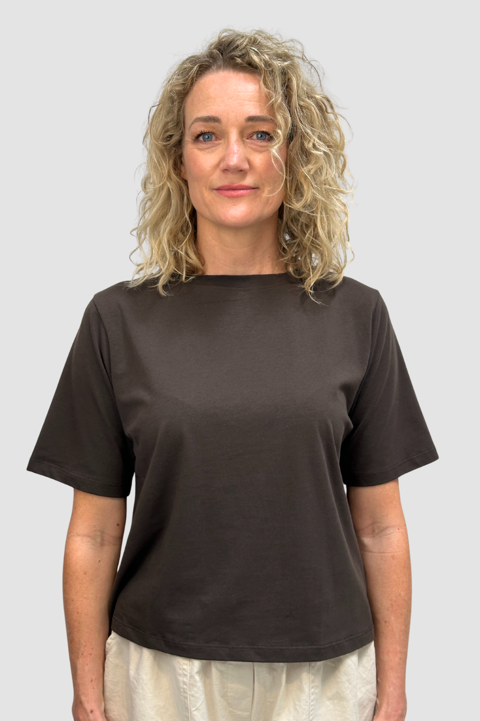 Woman with curly blonde hair wearing a dark brown organic cotton t-shirt against plain background