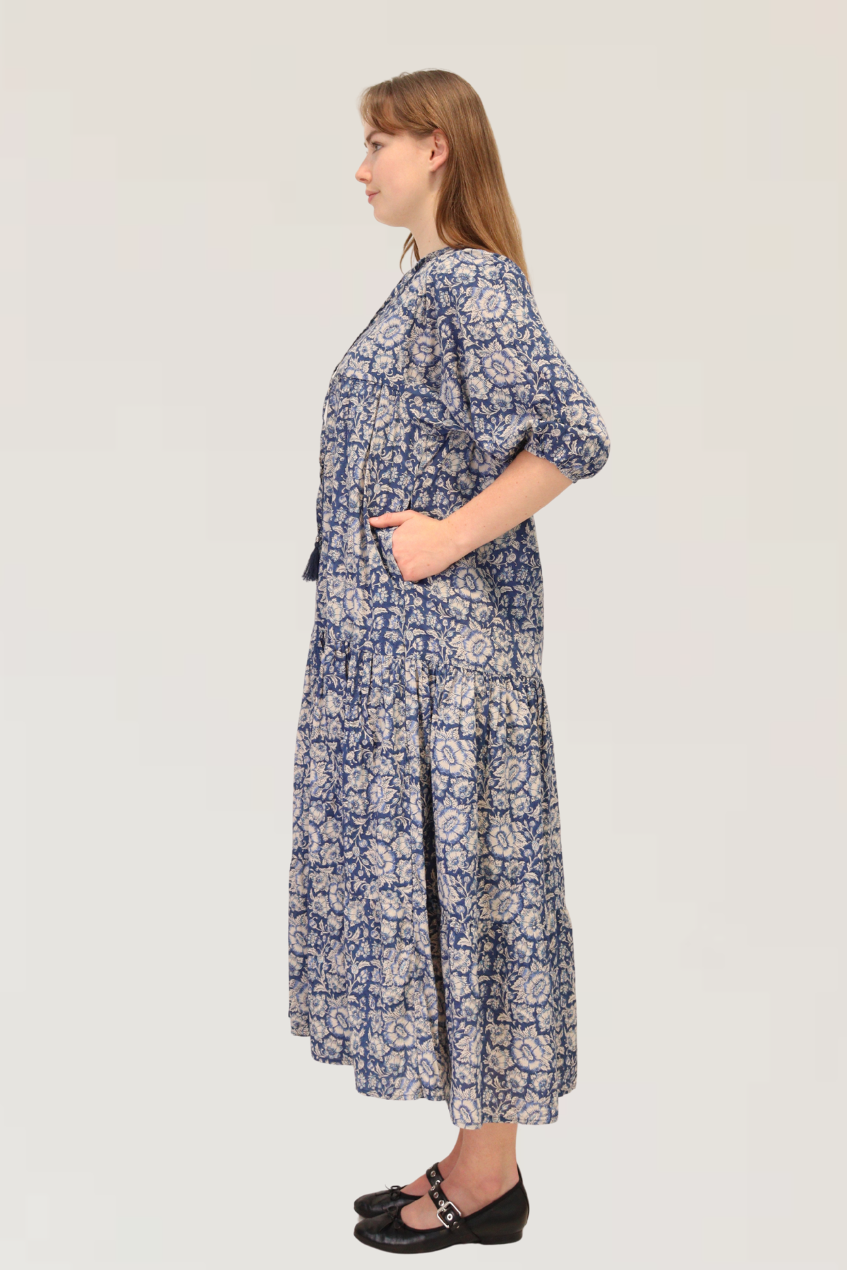 Side view of model wearing Serene Petals Maxi Dress in blue floral cotton, showing flowy tiered silhouette and side pockets.