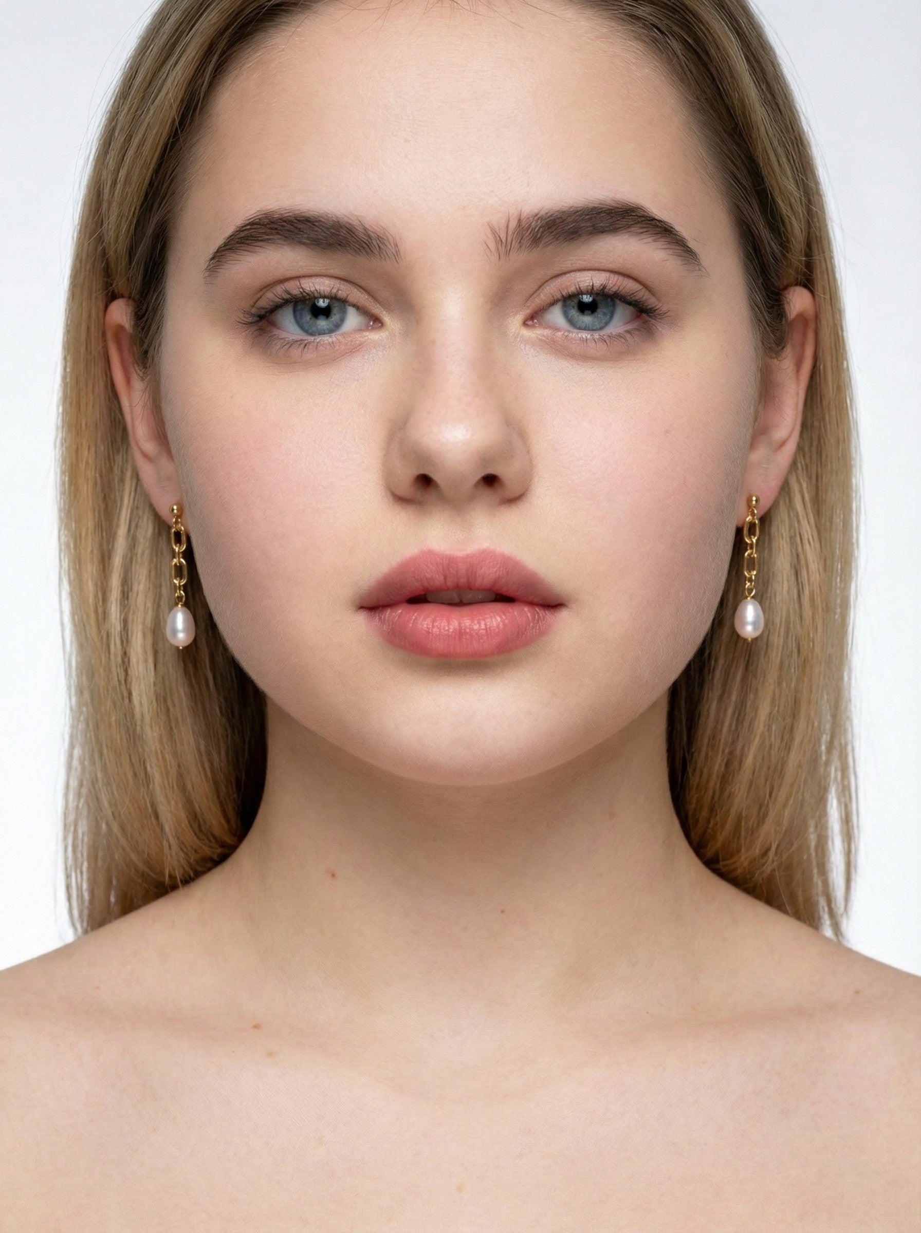 Close-up of a woman wearing pearl earrings with a plain background